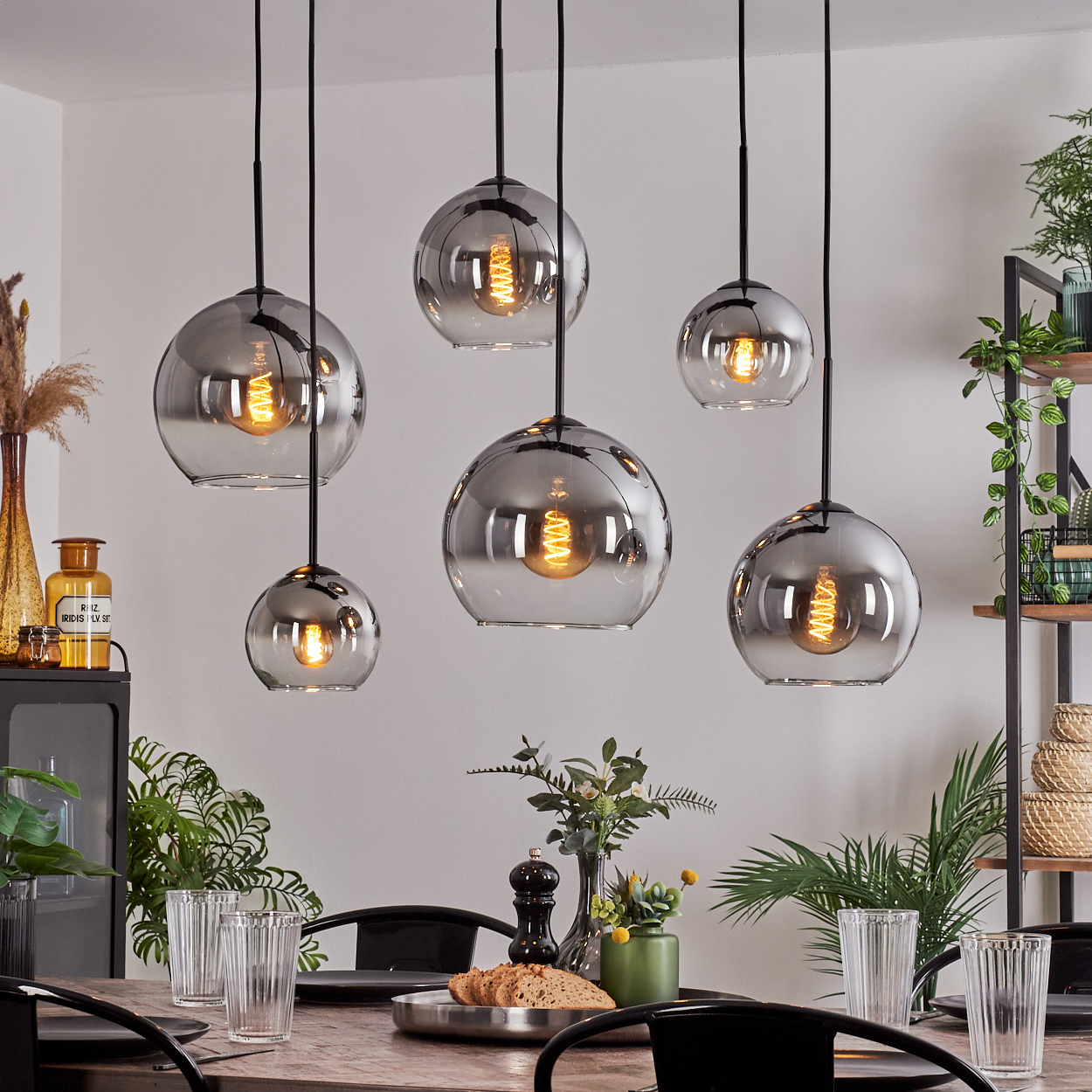 Mehrere Pendelleuchten mit Glaskugeln hängen über einem Esstisch. Die Leuchten haben Edison-Lampen.