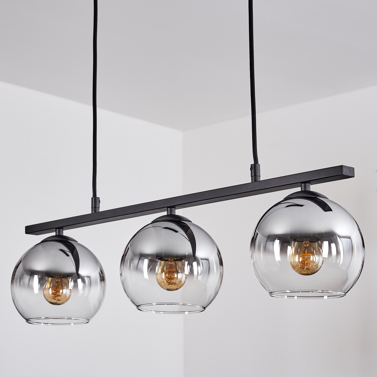 Drei Glas-Kugellampen, die an einer schwarzen Stange befestigt sind und von der Decke hängen.
