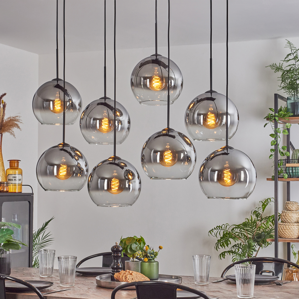 Neun Pendelleuchten mit Glaskugeln hängen über einem Tisch. Die Lichter sind an. Die Dekoration ist im Hintergrund.