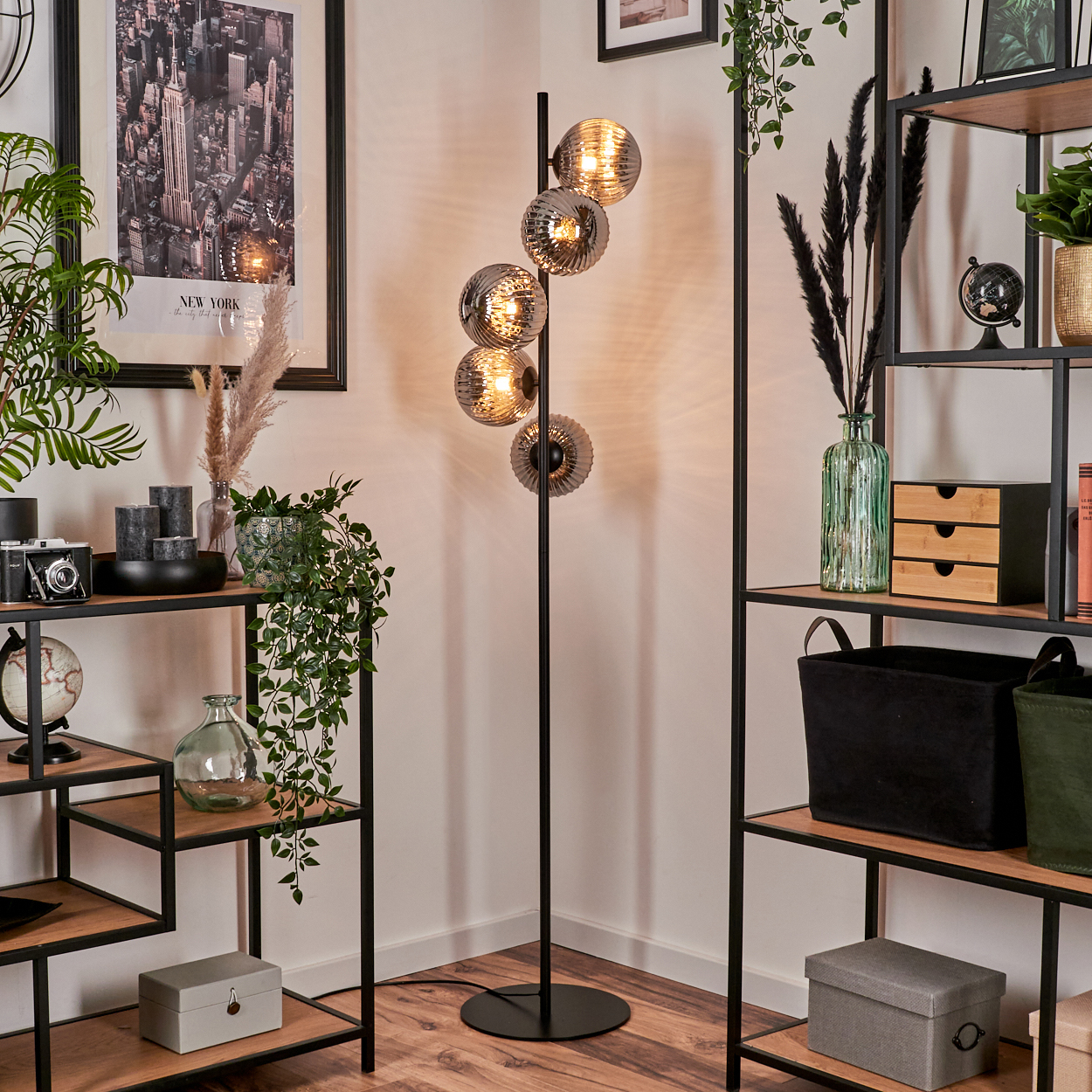 Eine Stehlampe mit fünf Glaskugeln. Regale mit Dekoration sind im Hintergrund. Die Lampe steht in einer Ecke.