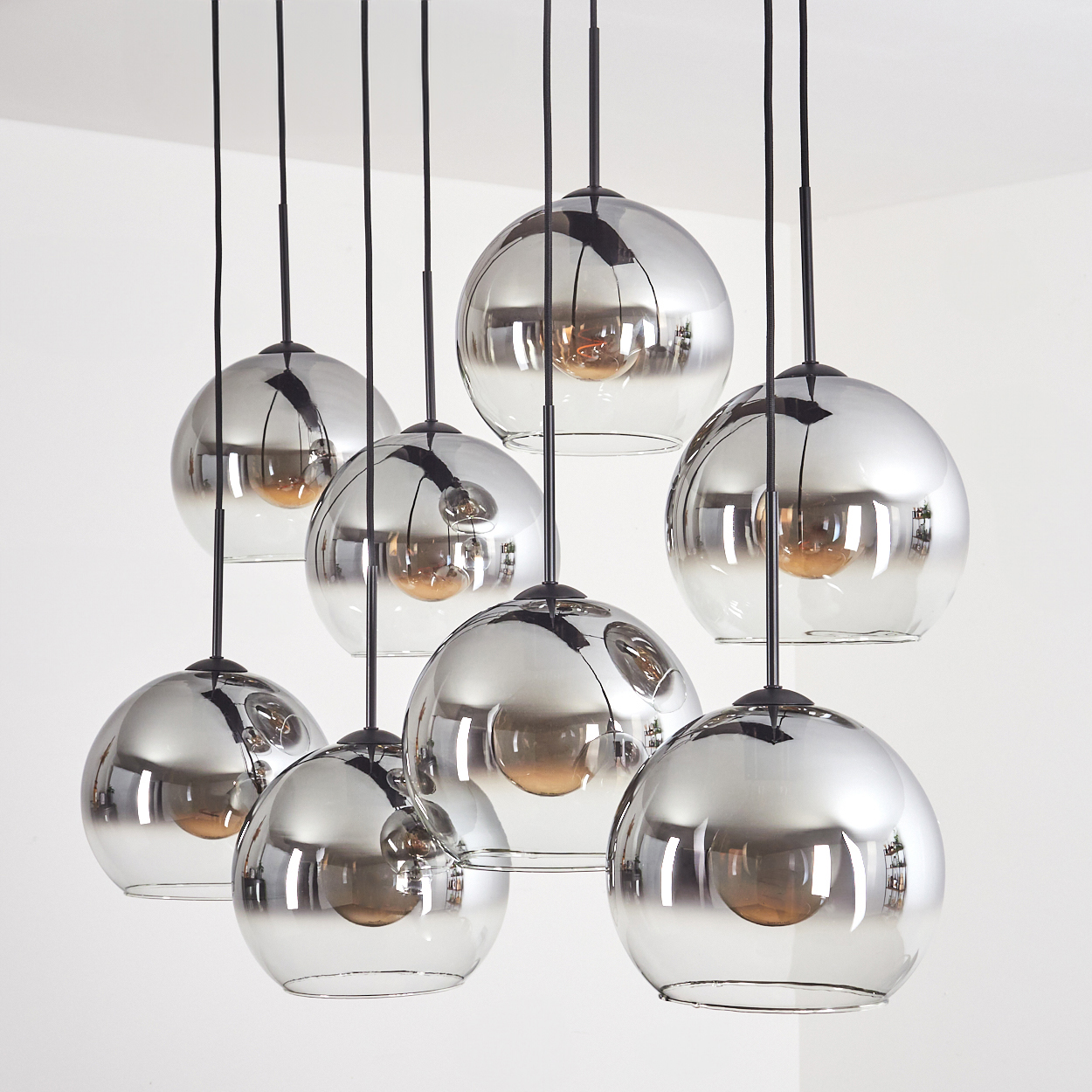 Neun silberne Glaskugellampen, die von der Decke hängen. Weißer Hintergrund.