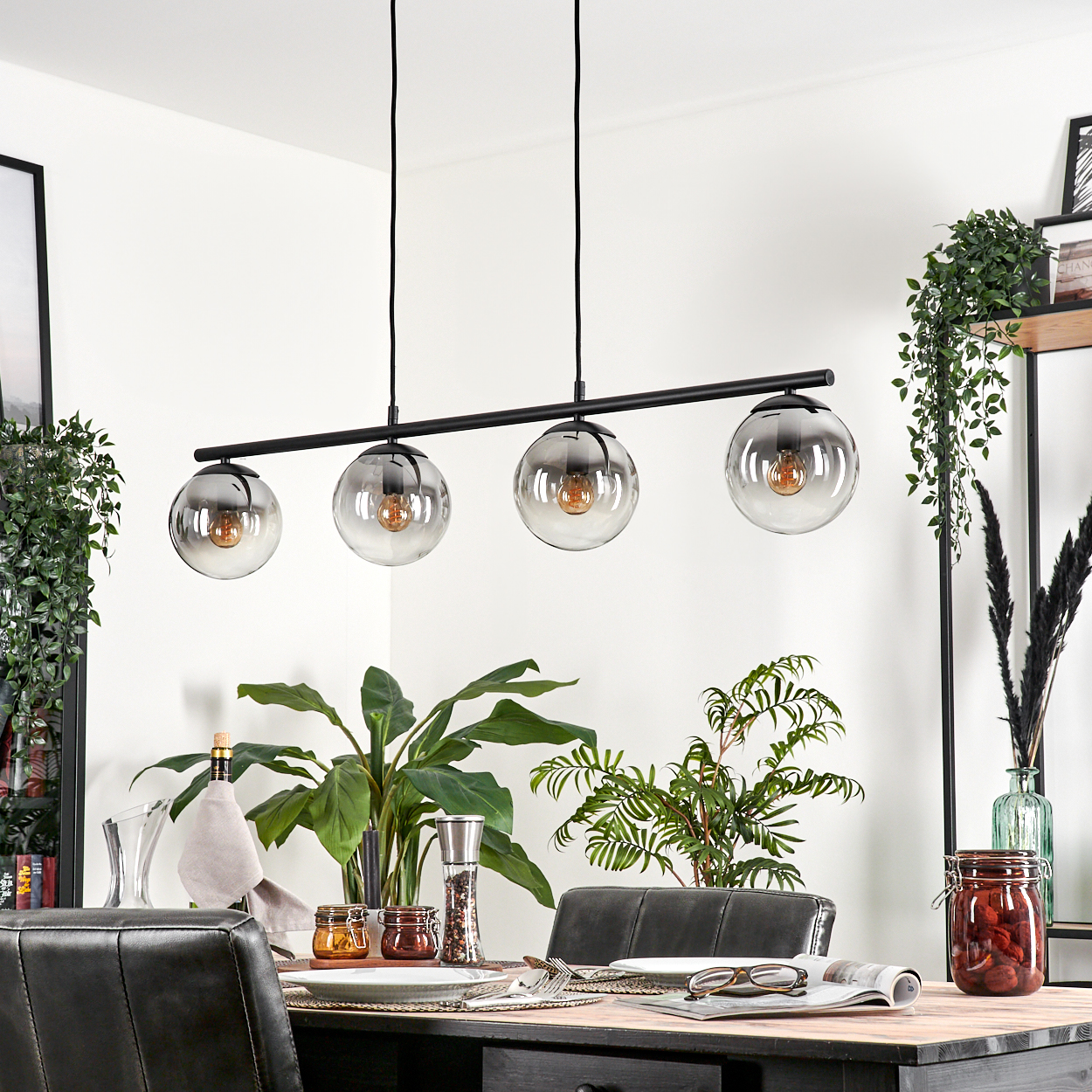 Ein Esszimmer mit einem schwarzen Kronleuchter mit 4 Glaskugeln, einem Tisch und Pflanzen.