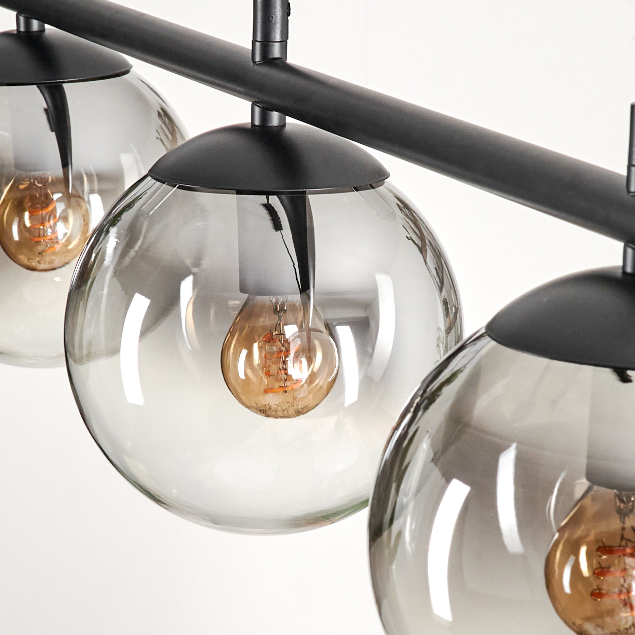 Nahaufnahme der Lampen, die die Glühbirnen im Inneren zeigen. Die Lampen sind aus klarem Glas und hängen an einer schwarzen Stange.