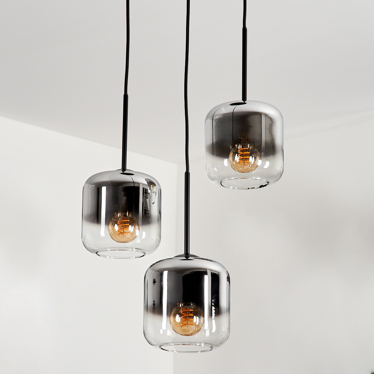 Drei Pendelleuchten mit transparenten Glasschirmen hängen in einer Inneneinrichtung. Glühbirnen sind sichtbar.