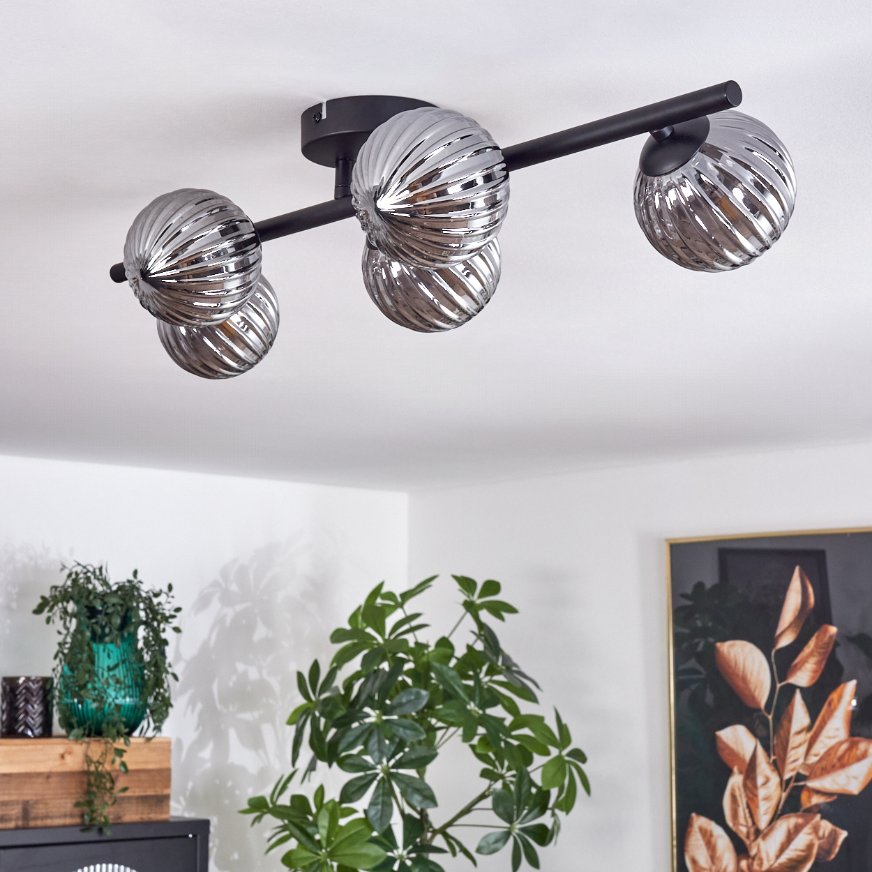 Eine Deckenlampe mit drei geriffelten Glaskugel-Schirmen, montiert auf einem schwarzen Rahmen. Innenraum.