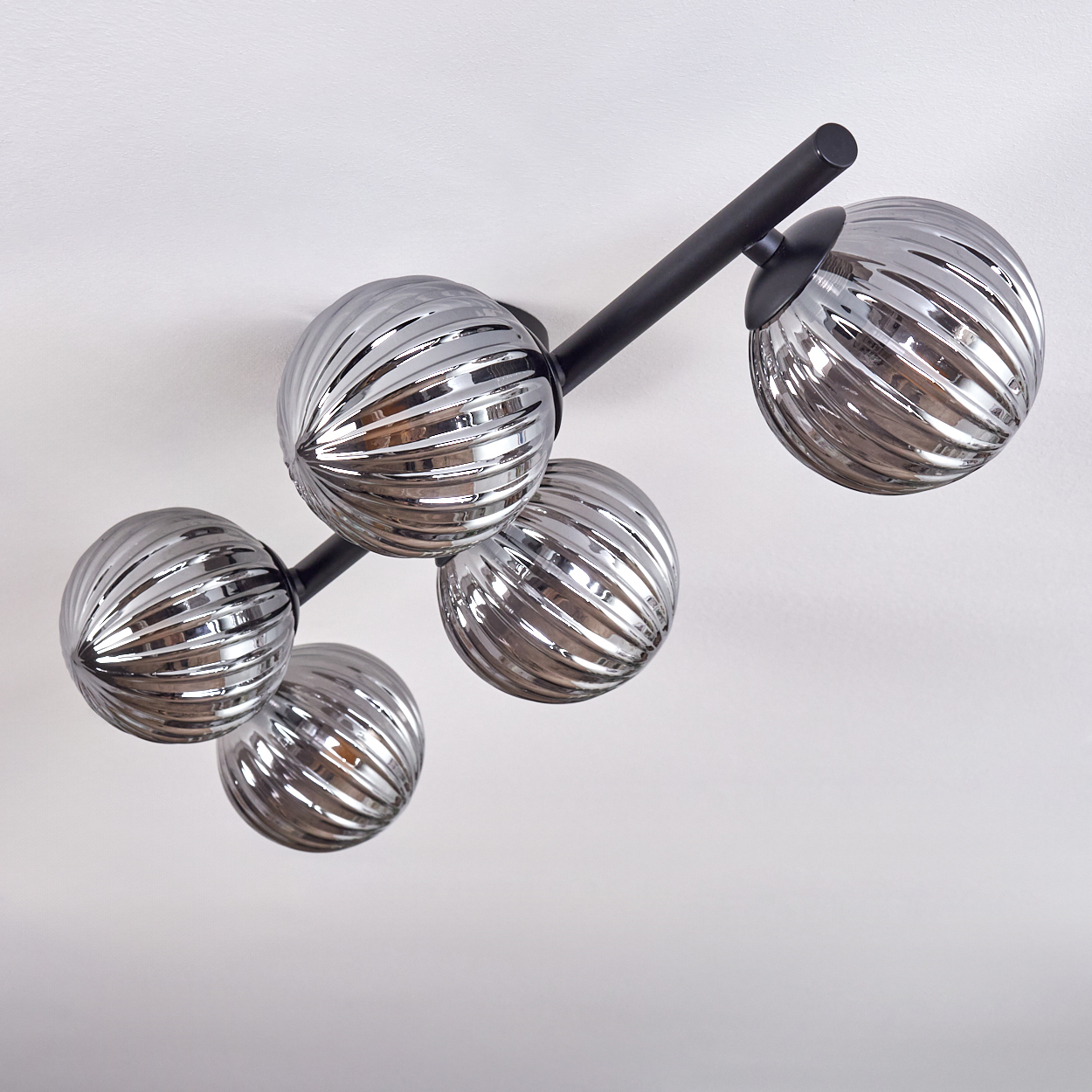 Eine Deckenlampe mit fünf geriffelten Glaskugeln und einer schwarzen Halterung. Der Hintergrund ist weiß.