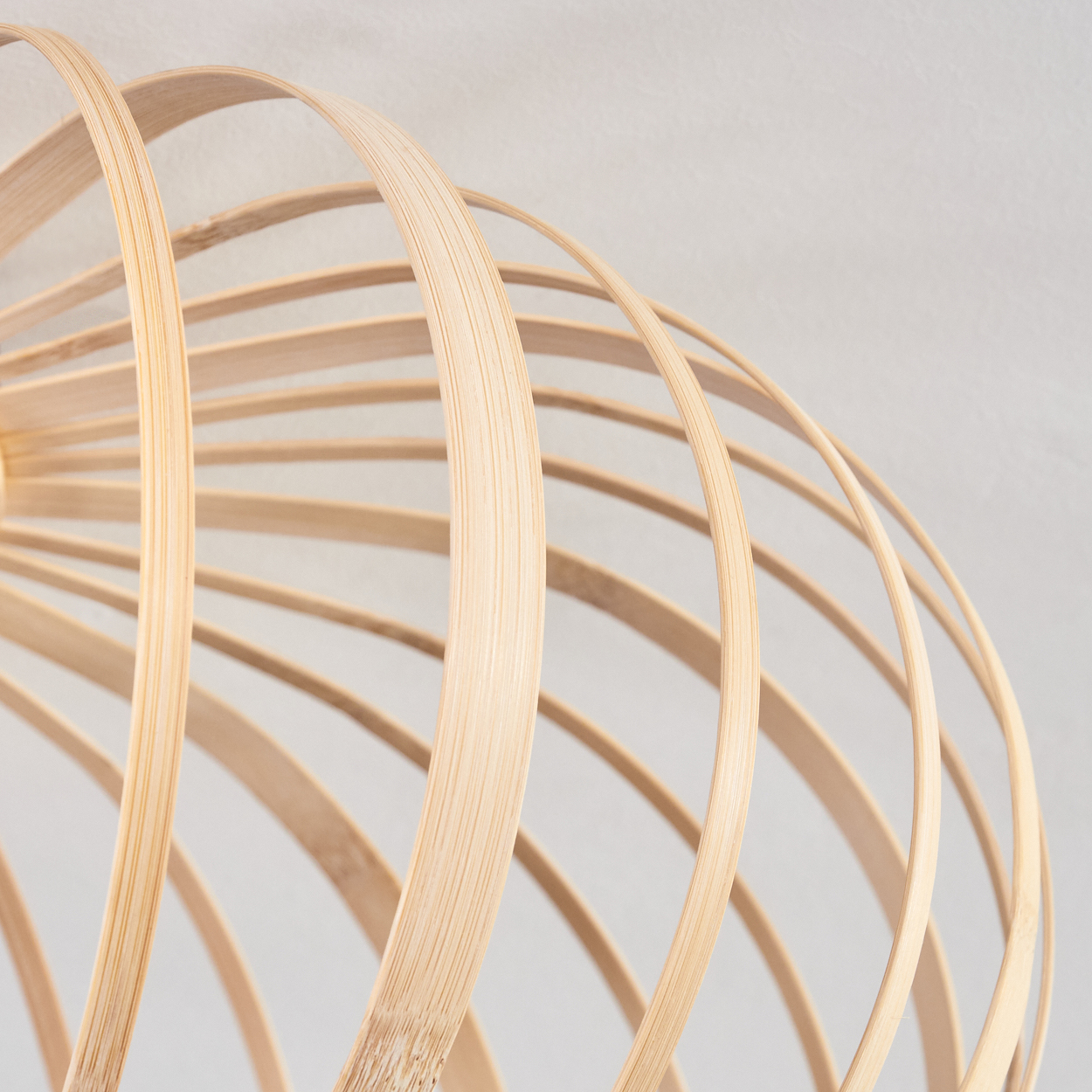 Nahaufnahme einer hellfarbigen Bambuslampe. Die Lampe hat eine runde Form und besteht aus gebogenen Bambusstreifen.