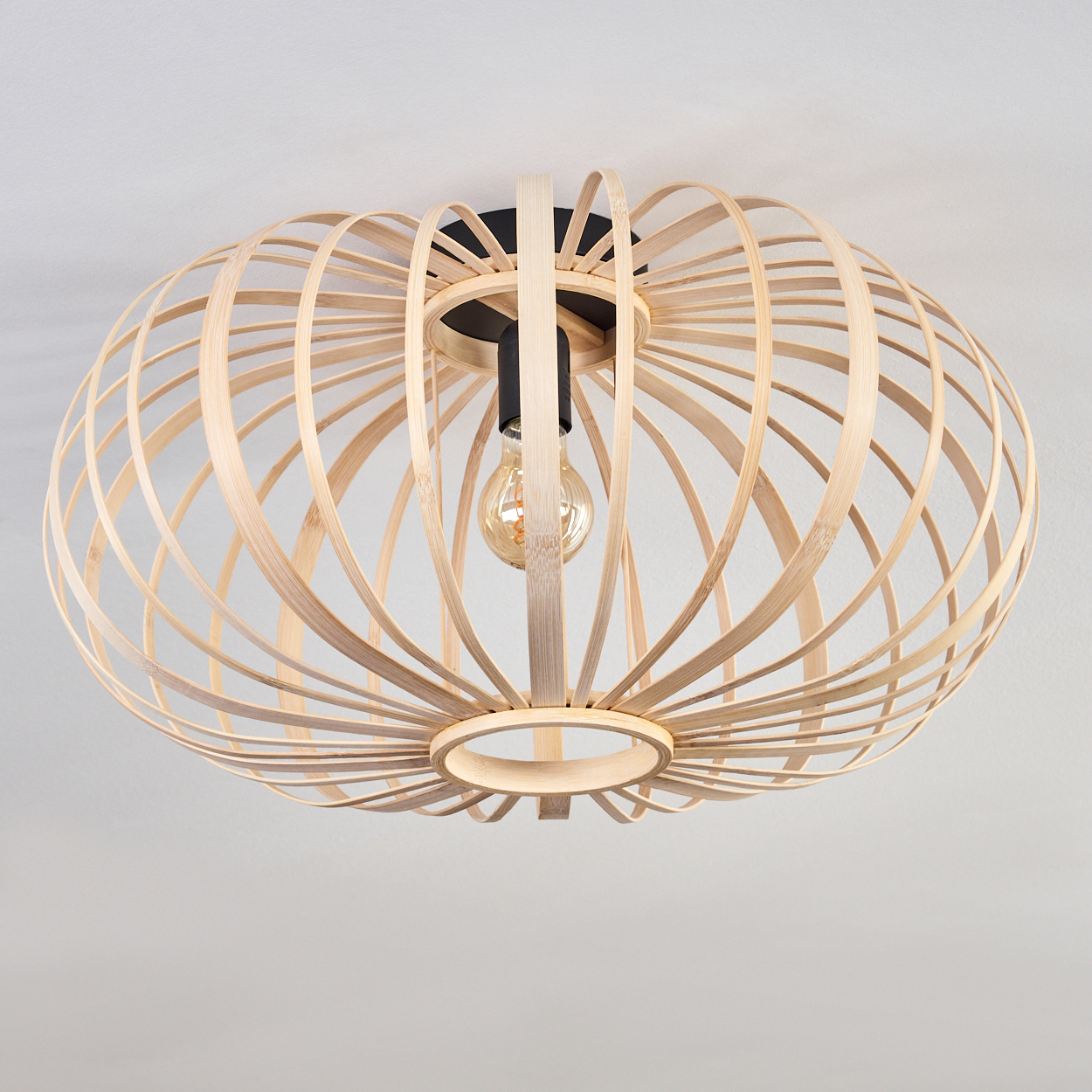 Eine Bambus-Deckenleuchte mit einer Glühbirne im Inneren. Die Lampe ist rund und besteht aus gebogenen Bambusstreifen.