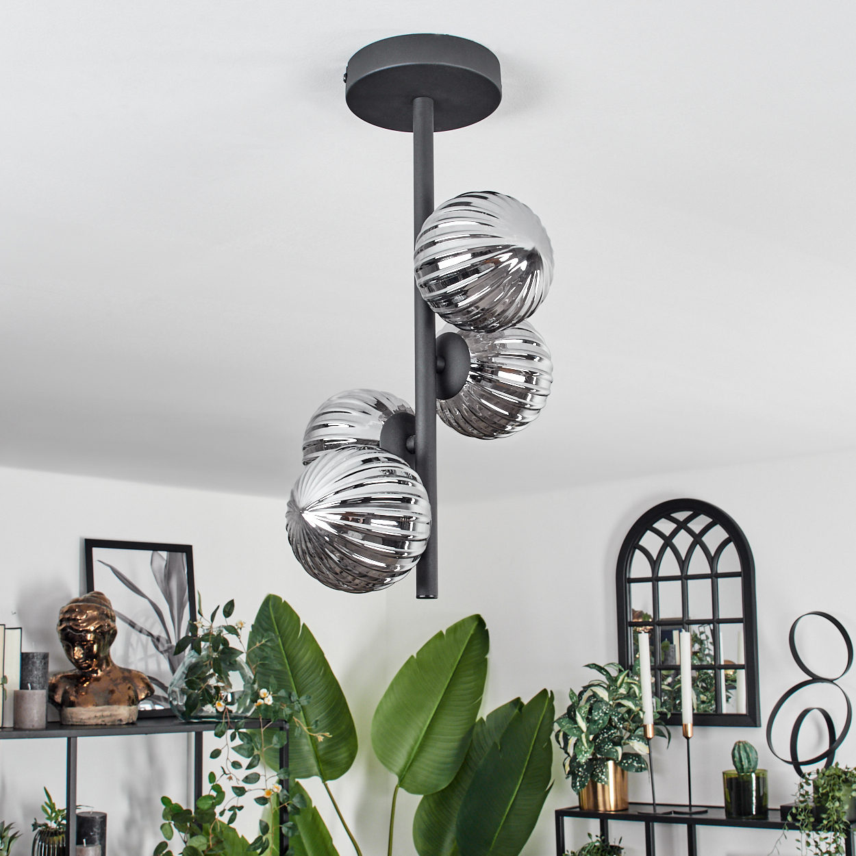 Moderne Deckenleuchte mit vier silbernen, gerippten Glaskugeln. Sie befindet sich in einem Raum mit Pflanzen, Regalen und Kunstwerken.