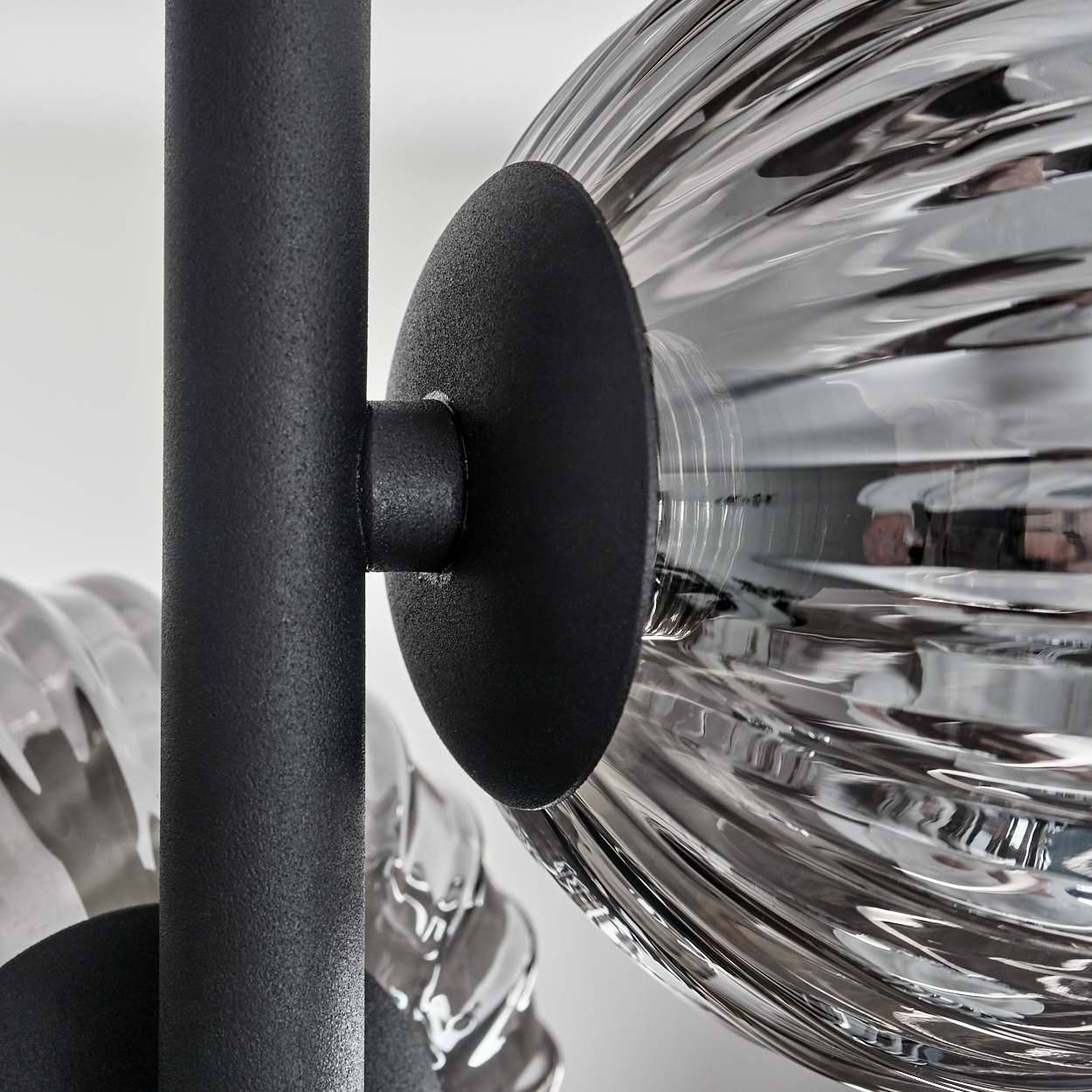 Nahaufnahme einer schwarzen Metallhalterung, die eine klare, geriffelte Glaskugel hält.