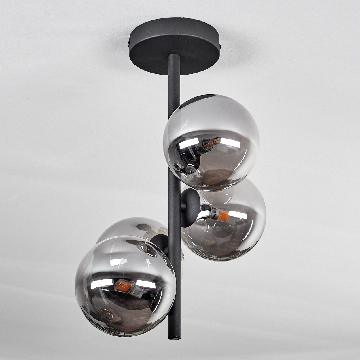 Moderne Deckenlampe mit vier verchromten Kugeln, die den Raum reflektieren, an einem schwarzen Stiel hängend.
