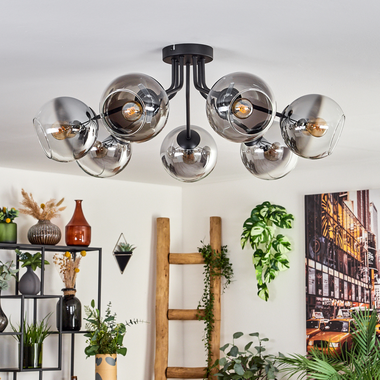 Eine Deckenlampe mit mehreren verchromten Kugeln und Lichtern, die von einer weißen Decke hängen. Innenraum mit Pflanzen und Dekor.