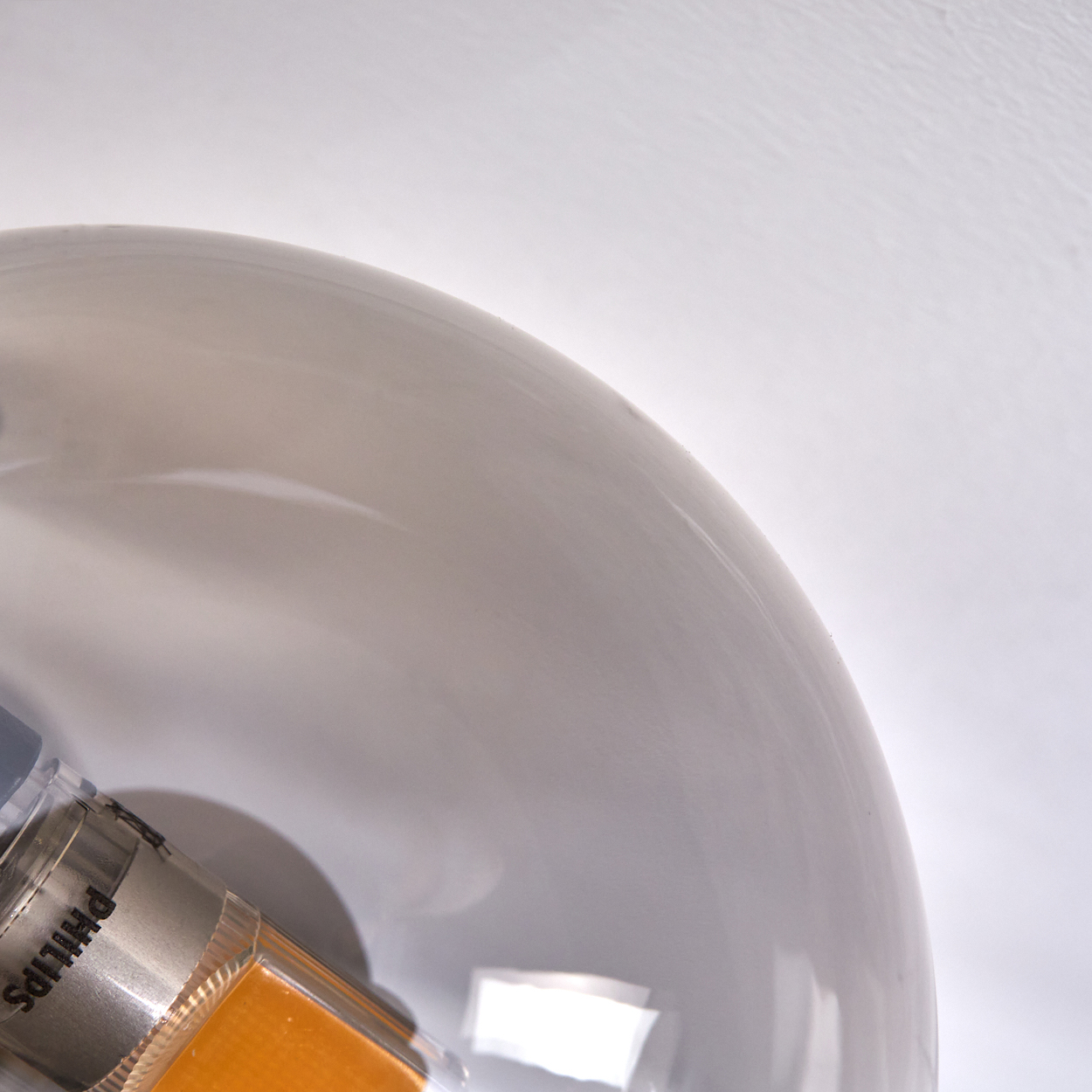 Nahaufnahme einer modernen Glaskugelleuchte. Silberne Metallbasis mit gelber Lichtquelle.