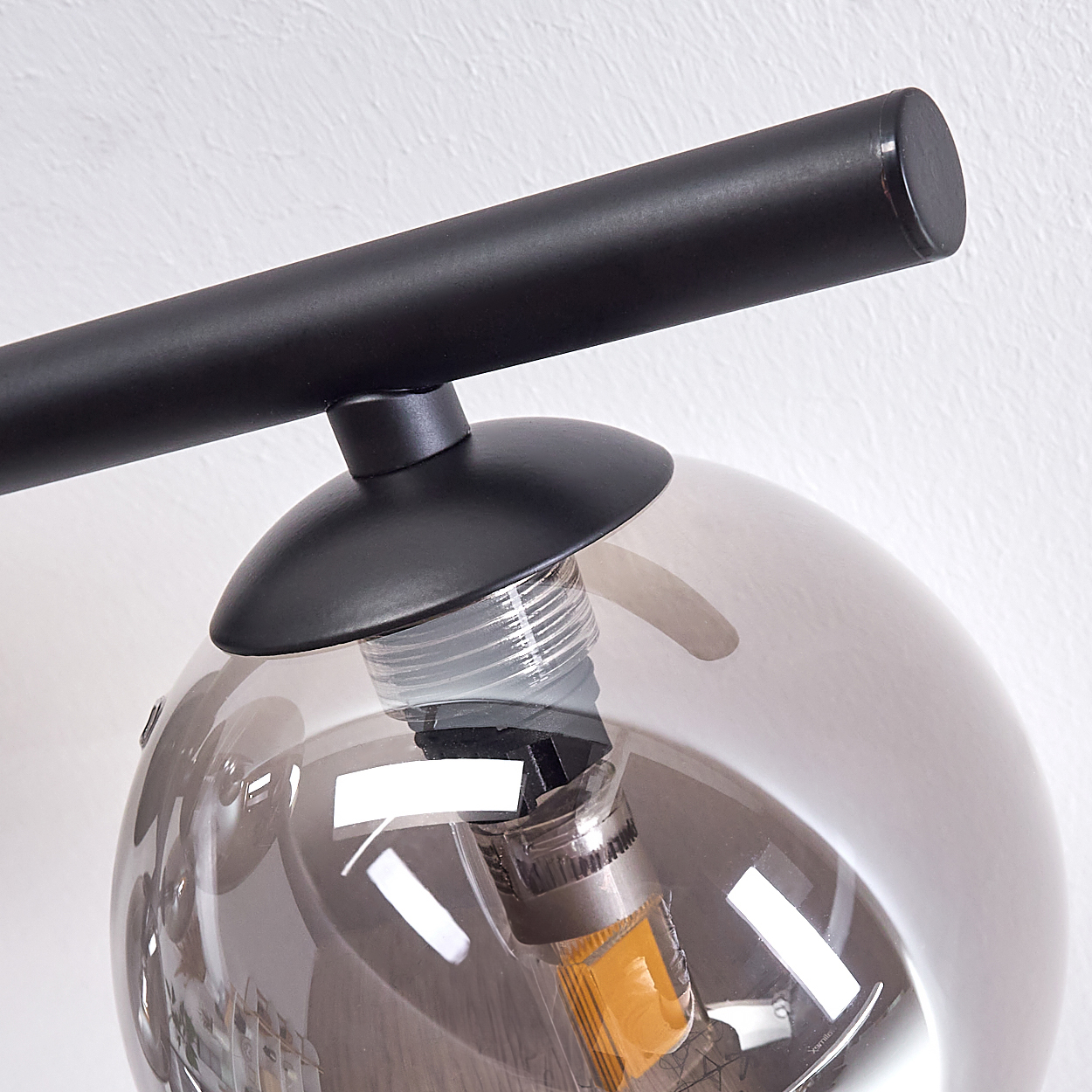 Nahaufnahme einer modernen Glaskugelleuchte mit schwarzem Träger. Die Glühbirne hat eine gelbe Lichtquelle.