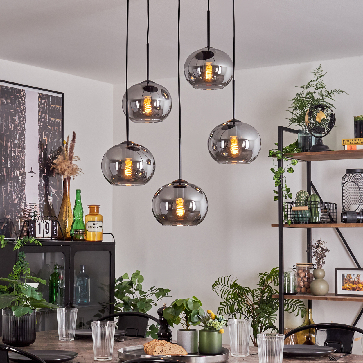 Fünf Pendelleuchten mit silbernen Kugeln über einem Tisch, mit einem Esszimmer im Hintergrund.