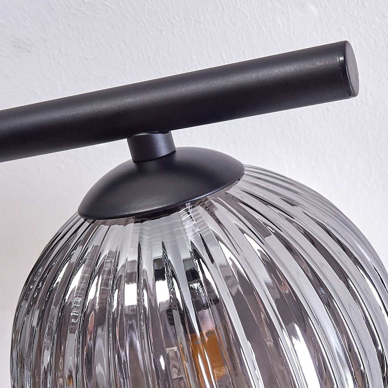 Nahaufnahme einer grauen Glaslampe mit schwarzem Metallarm. Die Lampe ist gerippt und reflektiert Licht.