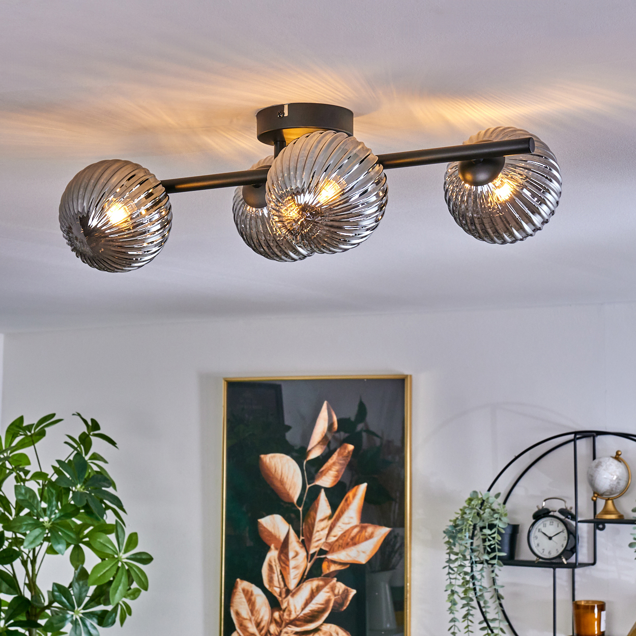 Deckenlampe mit drei grauen, gerippten Glaskugeln. Auf der Wand darunter befindet sich ein Blattgemälde.