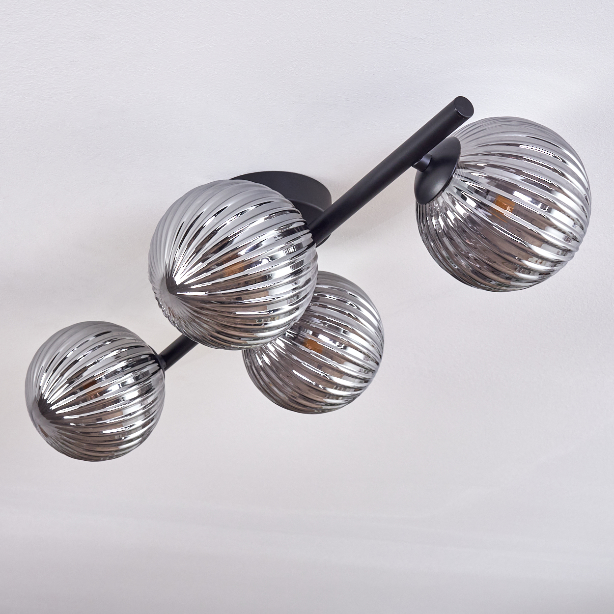 Deckenleuchte mit vier grauen, gerippten Glaskugeln an schwarzen Metallarmen, an einer weißen Decke montiert.