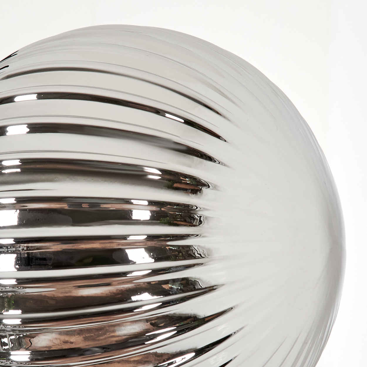 Nahaufnahme einer gerippten, silberfarbenen Glaskugel, die Licht reflektiert. Weißer Hintergrund.