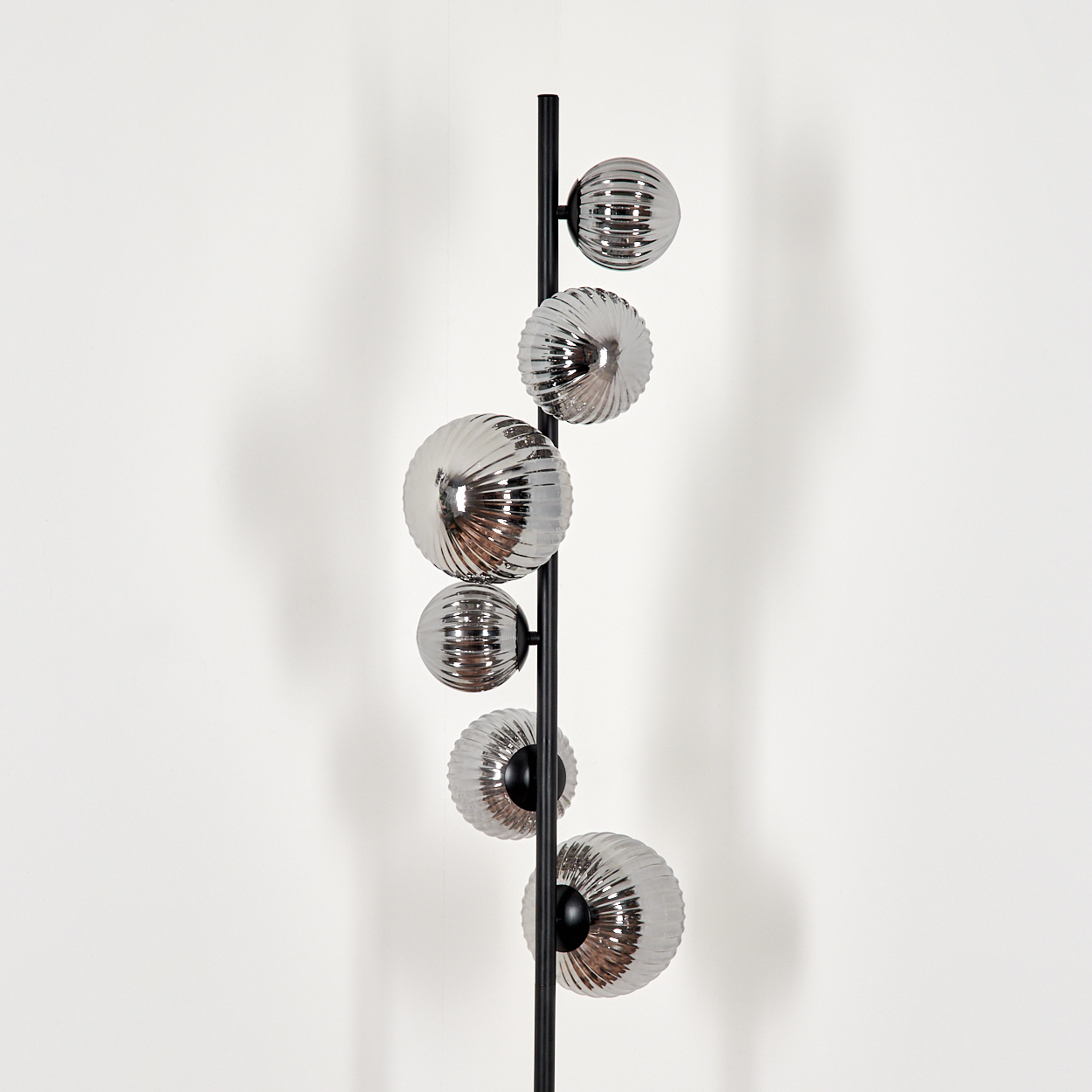 Eine Stehlampe mit sechs silbernen Kugelleuchten. Die Lampe hat einen schwarzen Metallmast. Der Hintergrund ist weiß.