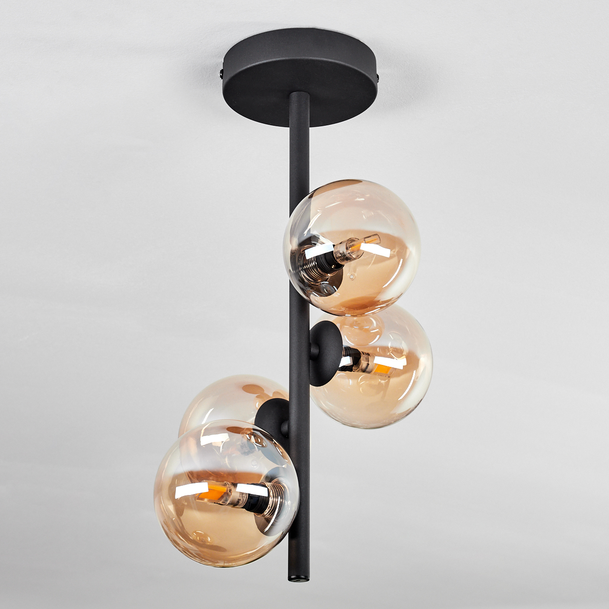 Eine Deckenlampe mit vier orangefarbenen Kugeln. Die Lampe hat einen schwarzen Stiel und einen schwarzen Sockel.