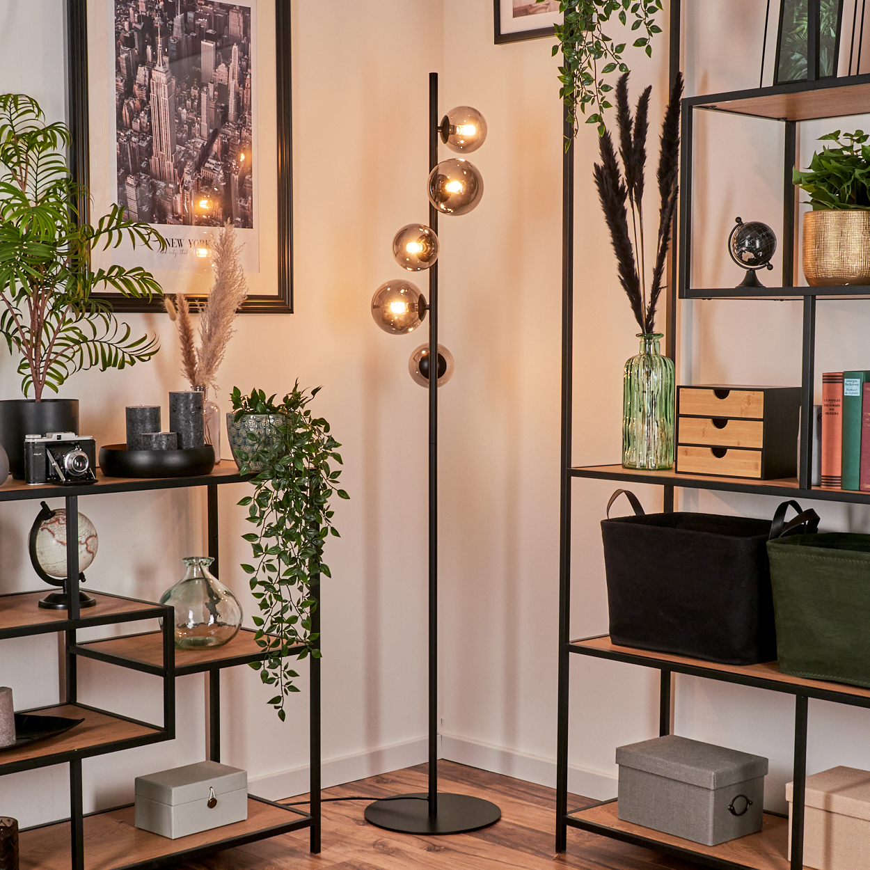 Ein Raum mit Regalen, Pflanzen und einer Stehlampe. Die Lampe hat fünf Glaskugeln. Der Hintergrund hat ein New York City Bild.
