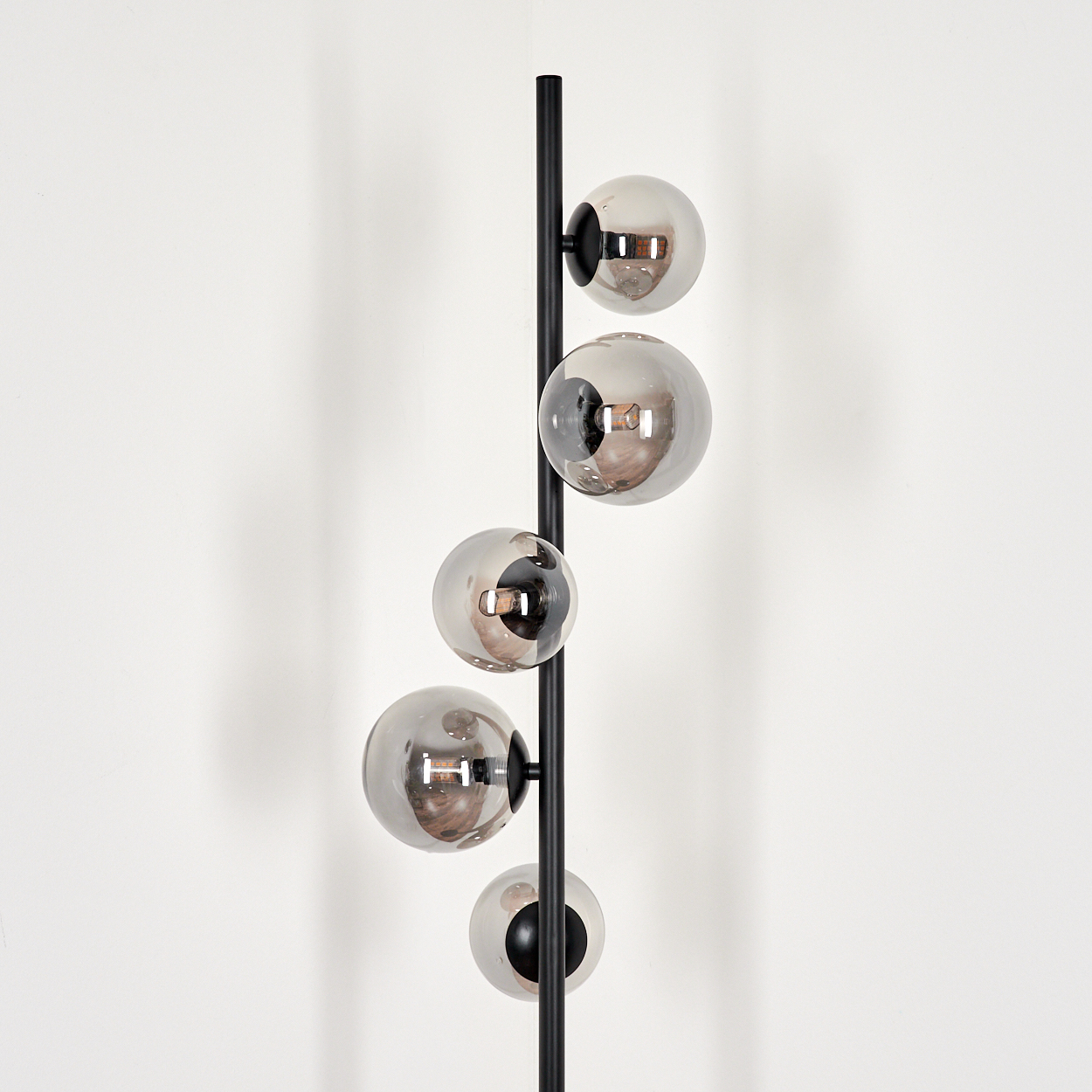 Eine Stehlampe. Es ist eine schwarze Stange mit fünf Glaskugeln. Der Hintergrund ist weiß.