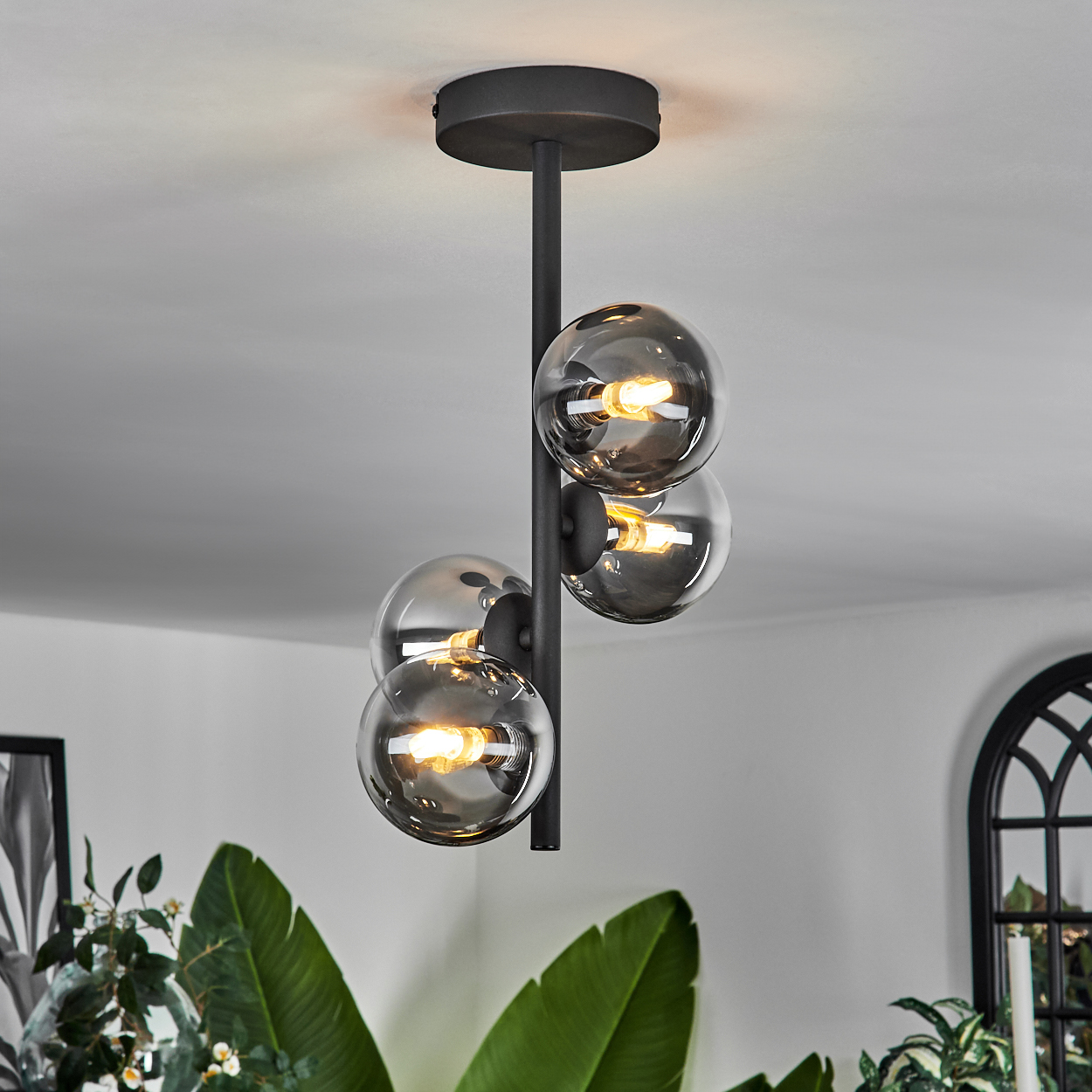 Eine Deckenlampe mit vier Glaskugeln. Ein schwarzer Rahmen ist sichtbar. Weißer Hintergrund.