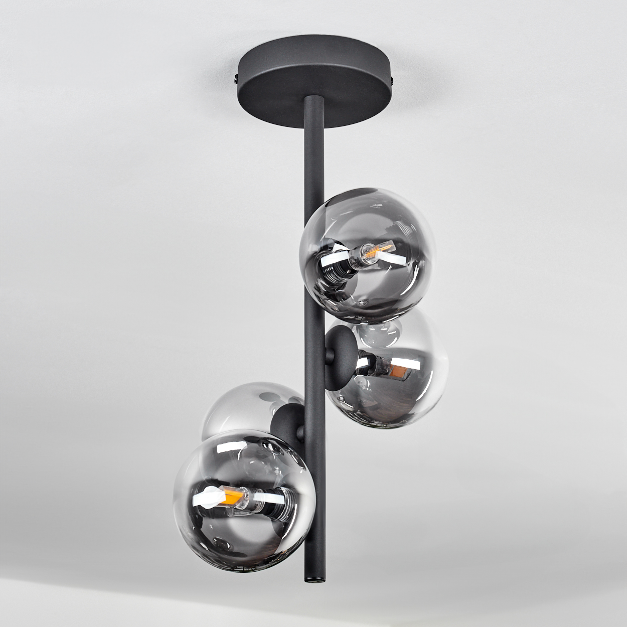Eine Deckenlampe mit vier Glaskugeln. Schwarzer Rahmen und weißer Hintergrund.