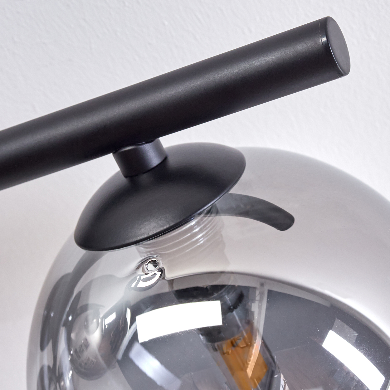 Nahaufnahme einer Deckenlampe. Ein schwarzer Rahmen und eine Glaskugel sind sichtbar.