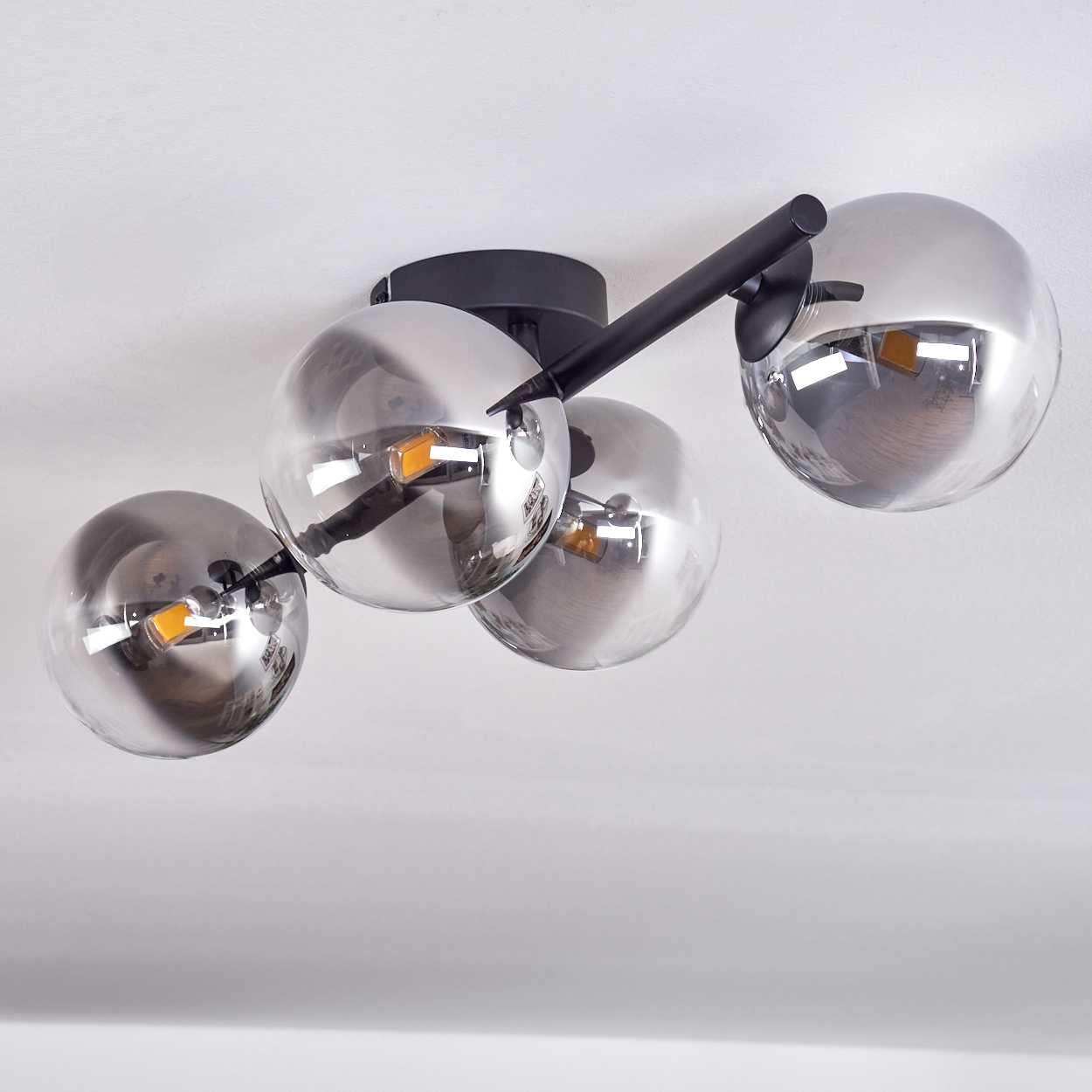 Eine Deckenlampe mit vier Glaskugeln. Schwarzer Rahmen und weißer Hintergrund.