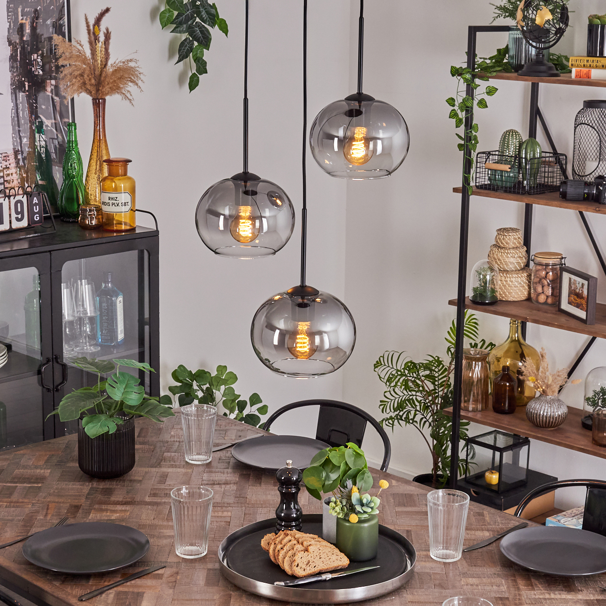 Esszimmer mit Holztisch und drei Pendelleuchten mit rauchfarbenen Glaskugeln.
