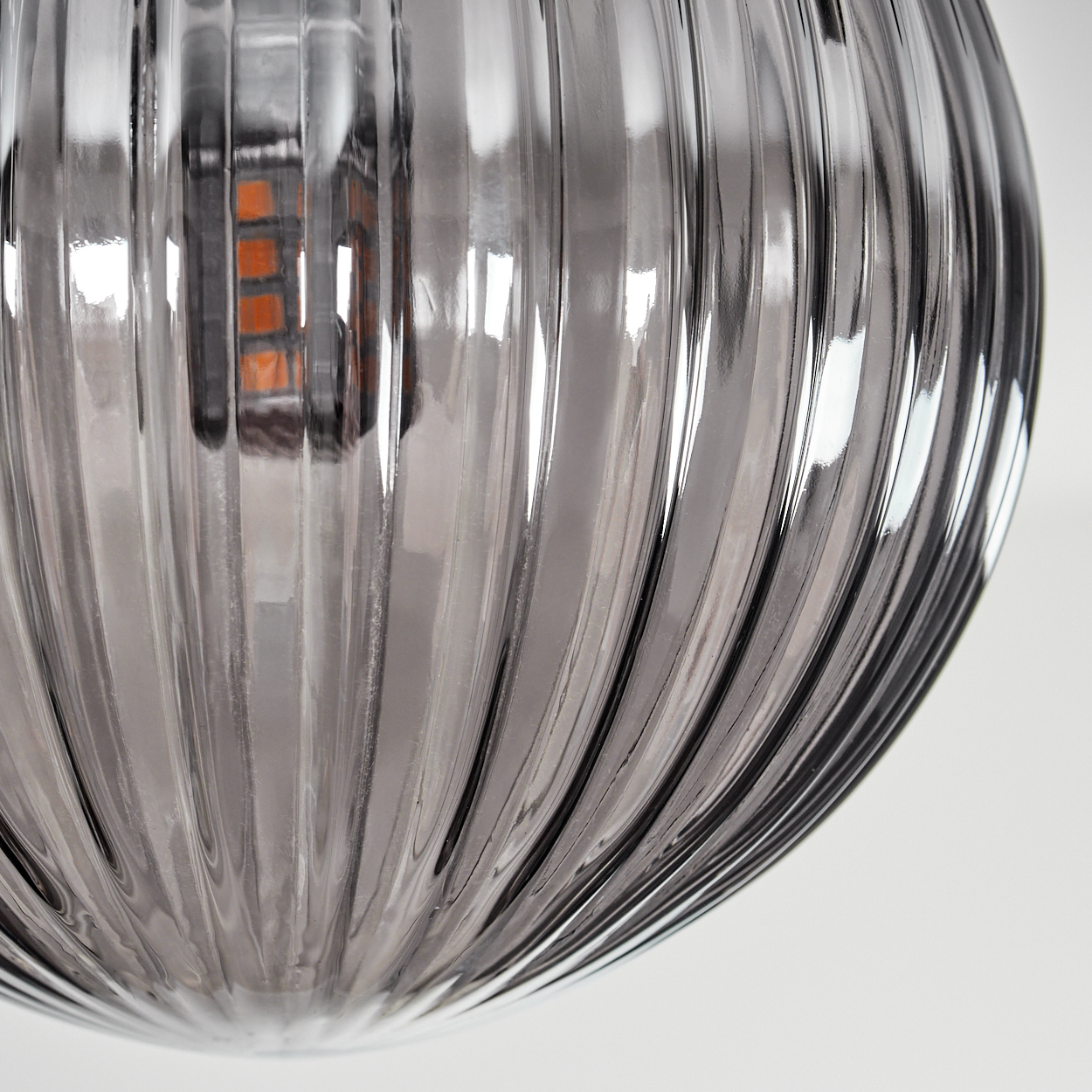 Nahaufnahme einer geriffelten Glaskugel. Das Glas ist transparent mit einer orangefarbenen Glühbirne darin.
