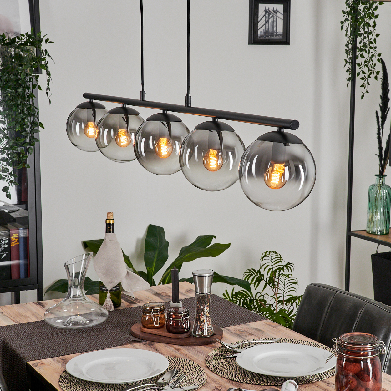 Esszimmer mit Holztisch und schwarzem Kronleuchter mit fünf transparenten Glühbirnen.