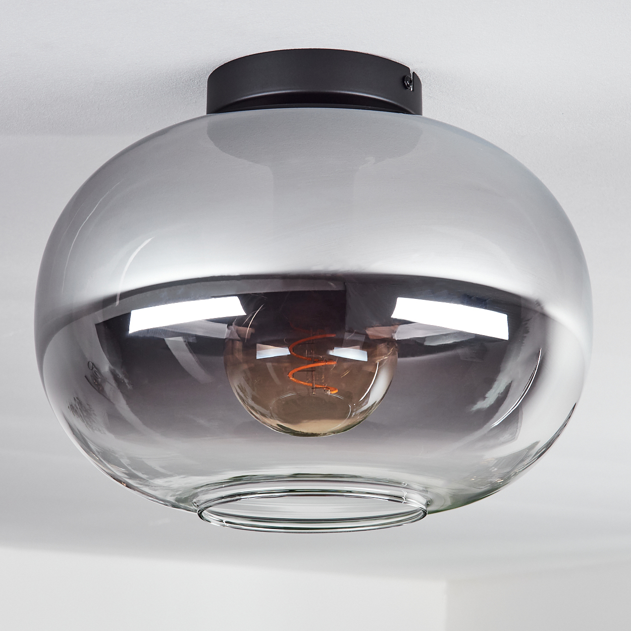 Eine runde, graue Glas-Deckenlampe mit sichtbarer Glühbirne hängt von einer weißen Decke ab.