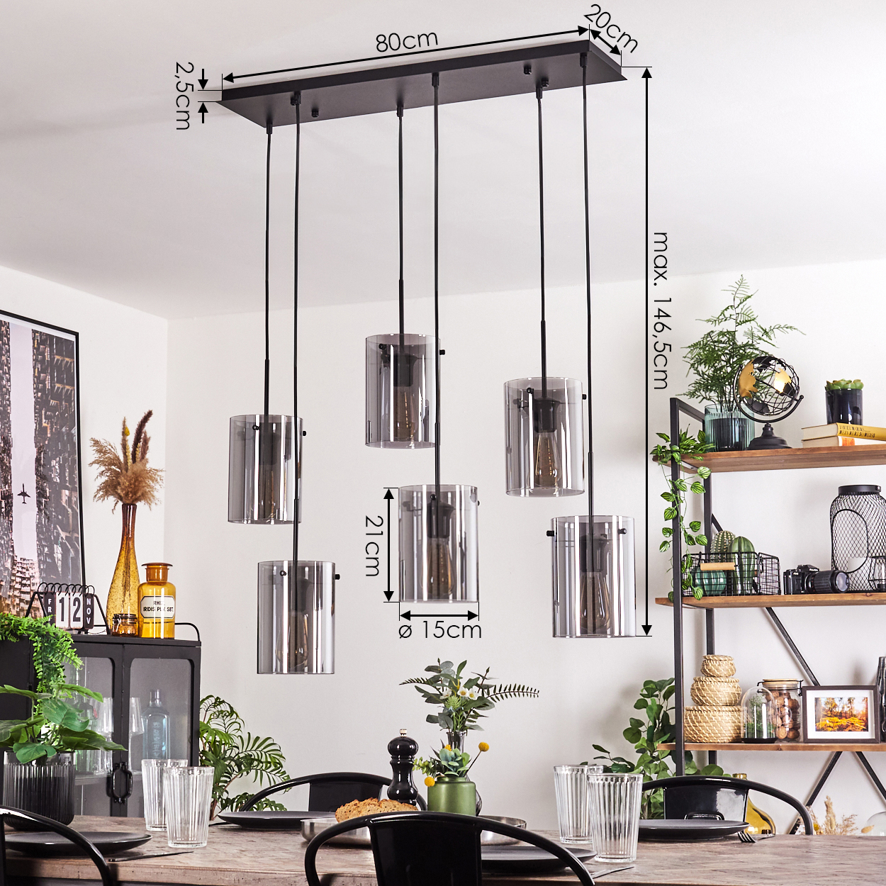 Esstisch mit sechs Pendelleuchten. Jede Lampe hat einen zylindrischen Glasschirm. Mit Deko.