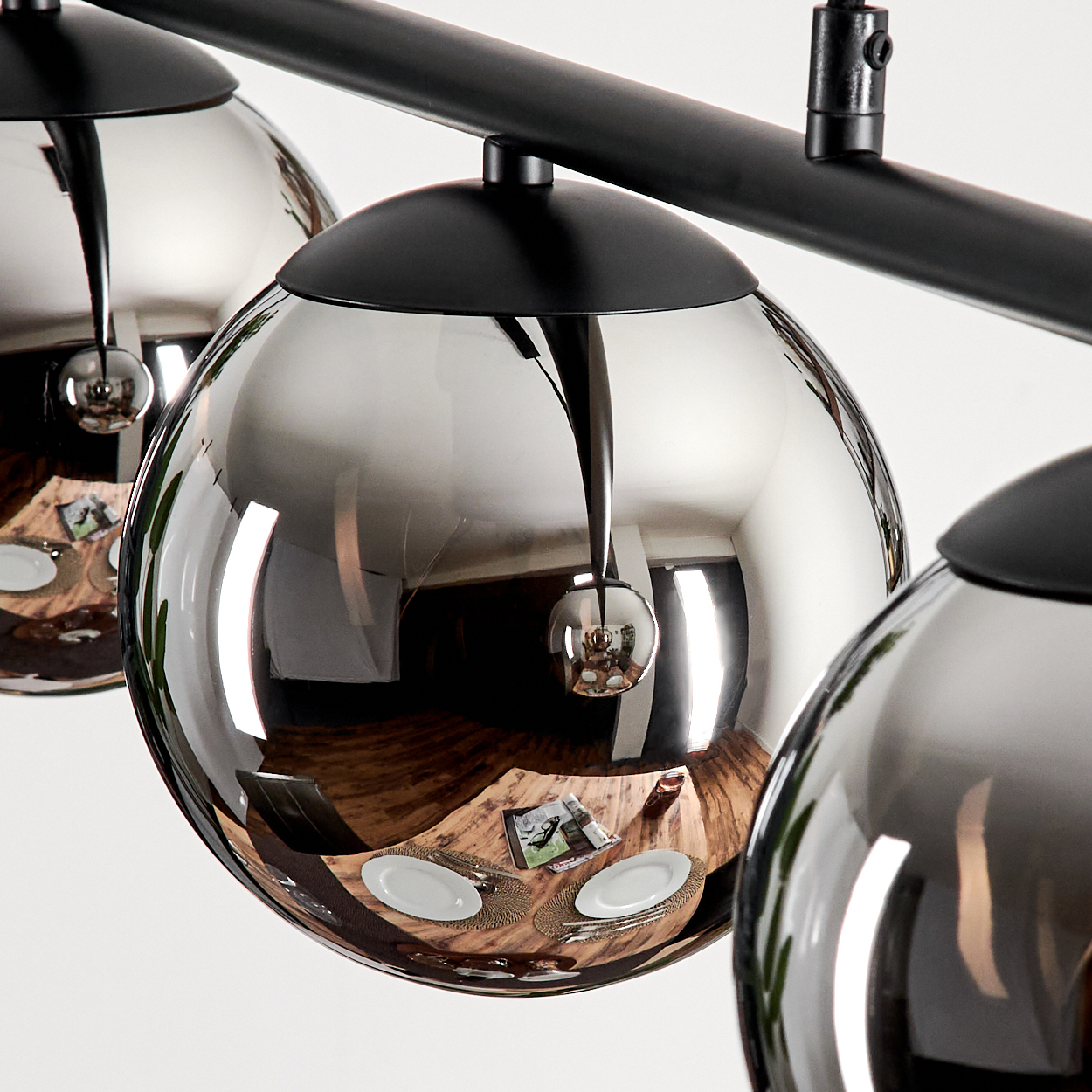 Nahaufnahme von Pendelleuchten mit reflektierenden Kugelschirmen. Reflektiert werden Raum und Tisch.