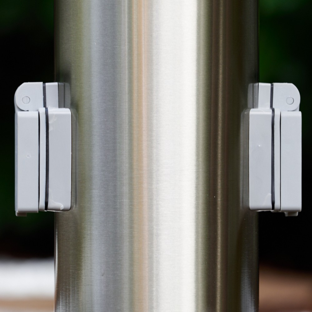 Nahaufnahme einer Metallsäule mit zwei grauen, rechteckigen Befestigungen. Dunkler Hintergrund.