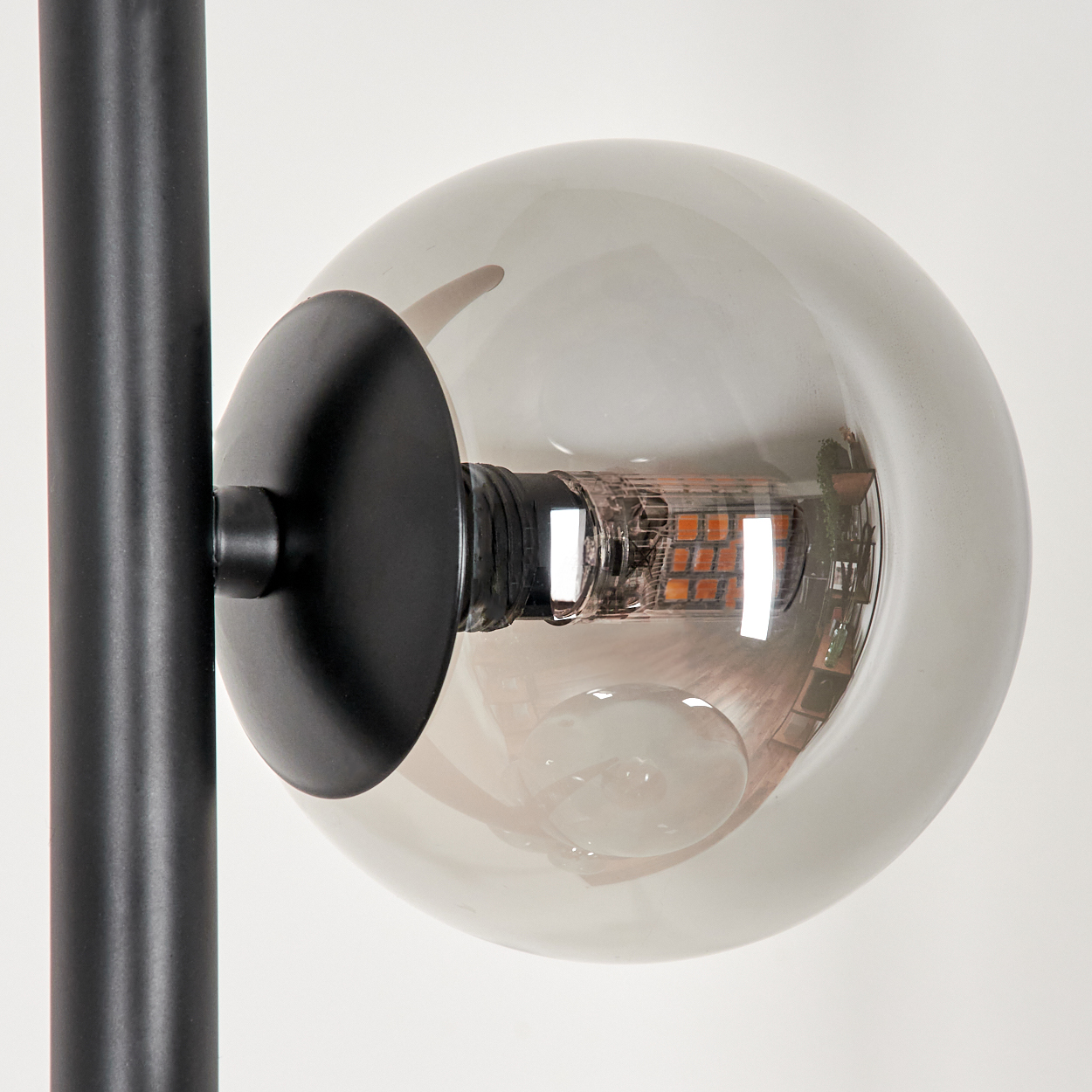 Nahaufnahme eines schwarzen Stiels und einer Glaskugel einer Lampe. Die Kugel hat eine Glühbirne im Inneren.