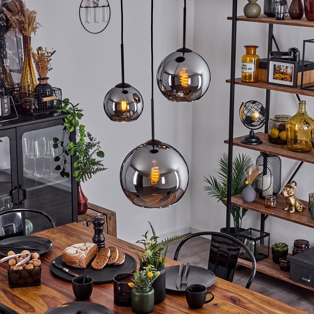 Esszimmer mit Holztisch, drei Pendelleuchten und einem schwarzen Schrank. Essen und Deko auf dem Tisch.
