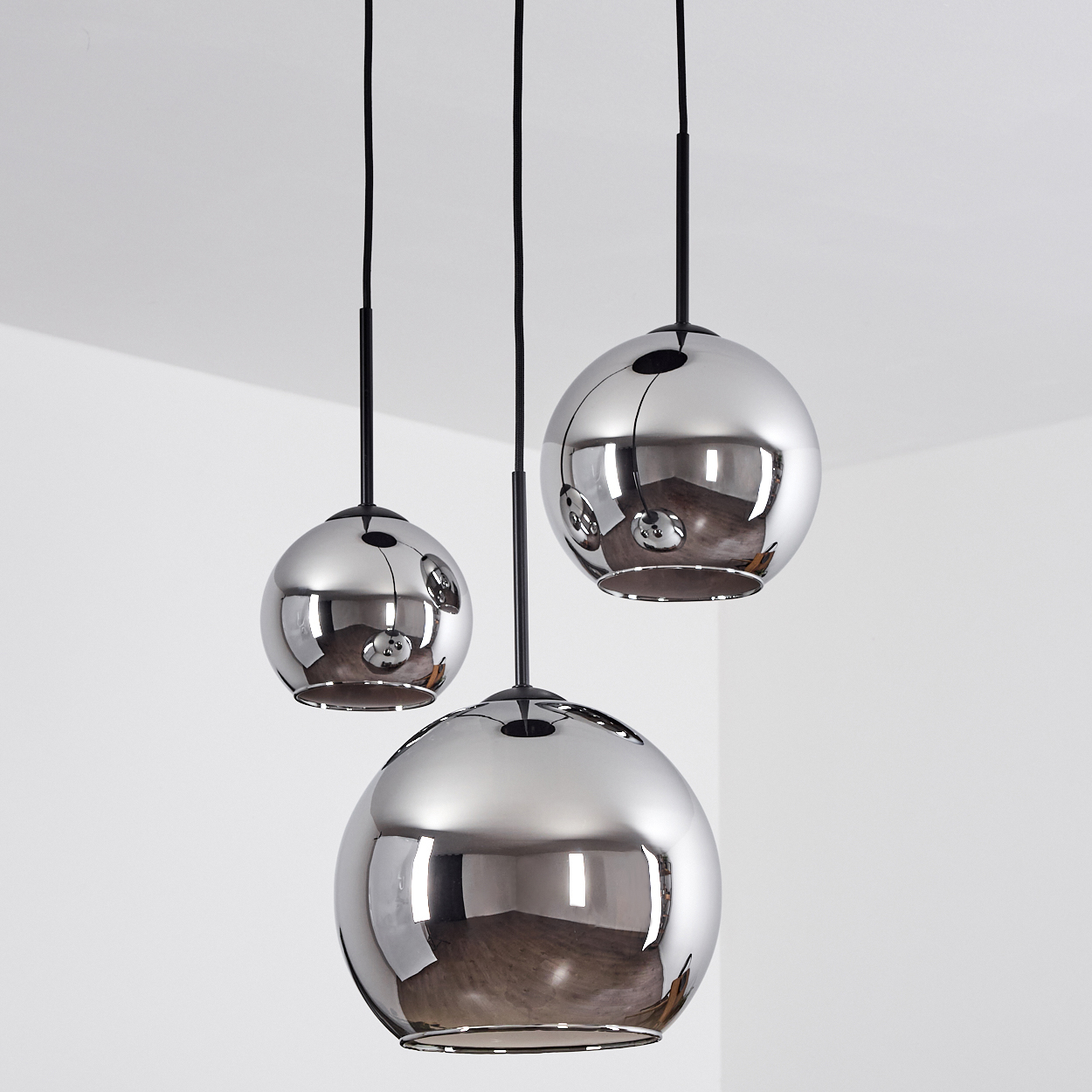 Drei Pendelleuchten mit silbernen Kugeln, die von der Decke hängen. Der Hintergrund ist eine schlichte weiße Wand.