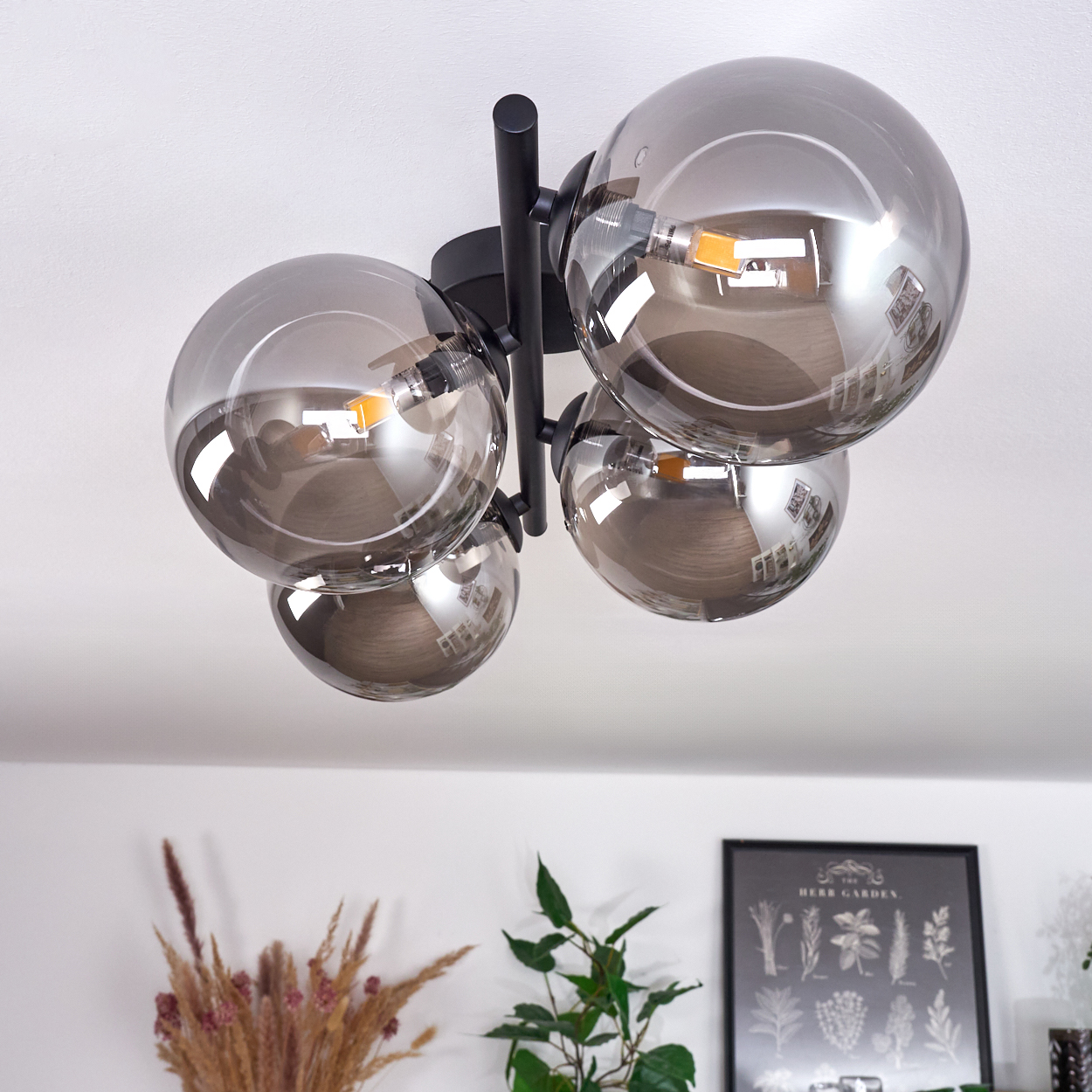 Eine Deckenlampe mit vier reflektierenden silbernen Kugeln. Die Lampe ist an einer weißen Decke montiert. Eine Zimmerecke sichtbar.