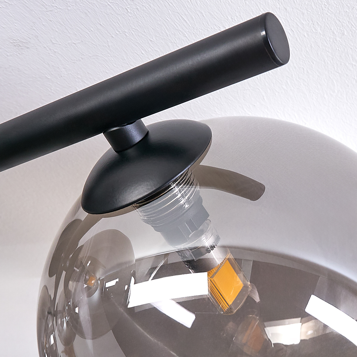 Nahaufnahme einer silbernen Kugelbirne und einer schwarzen Stangenverbindung. Die Kugel reflektiert Licht und einen Raum.
