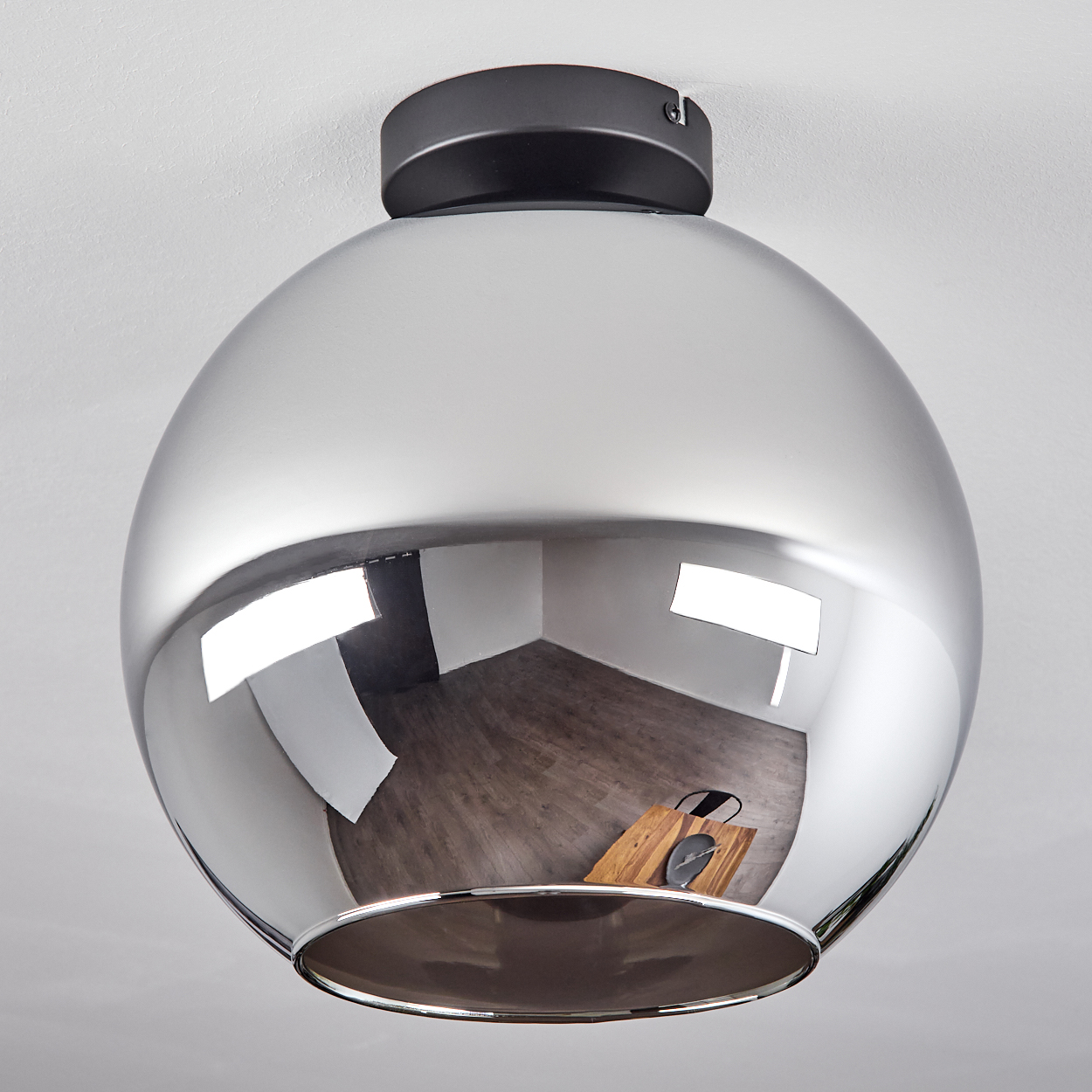 Eine verchromte Kugeldeckenlampe, die einen Rauminnenraum mit Holzboden und dunklem Tisch reflektiert.