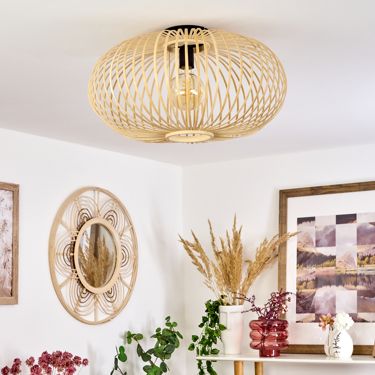 Eine Deckenlampe im Bambus-Stil. Ein Spiegel und Pflanzen im Hintergrund.