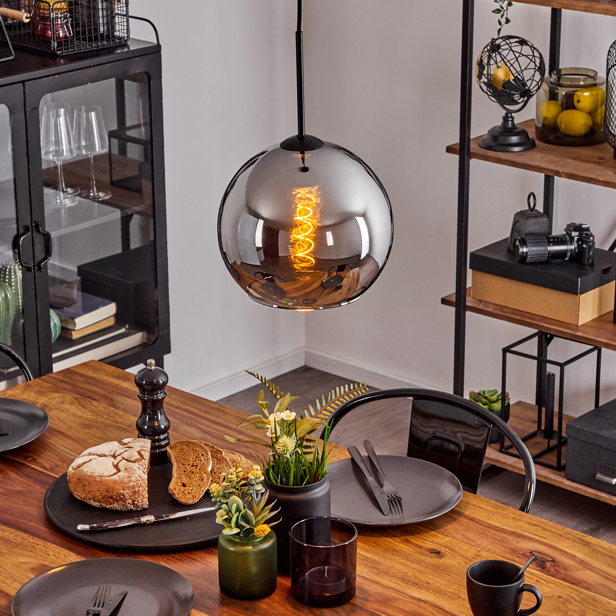 Esstisch mit Pendelleuchte. Eine kugelförmige Lampe hängt über der Tischdekoration.
