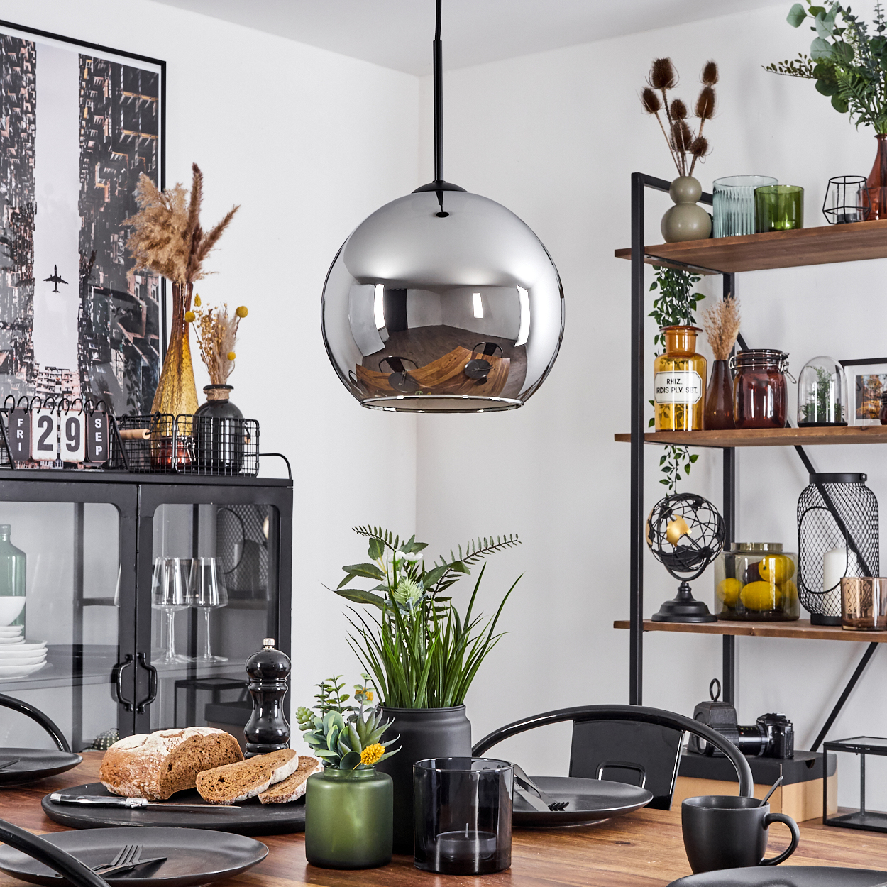 Ein Esszimmer mit Holztisch, schwarzen Stühlen, Hängelampe und dekorativen Gegenständen auf Regalen.