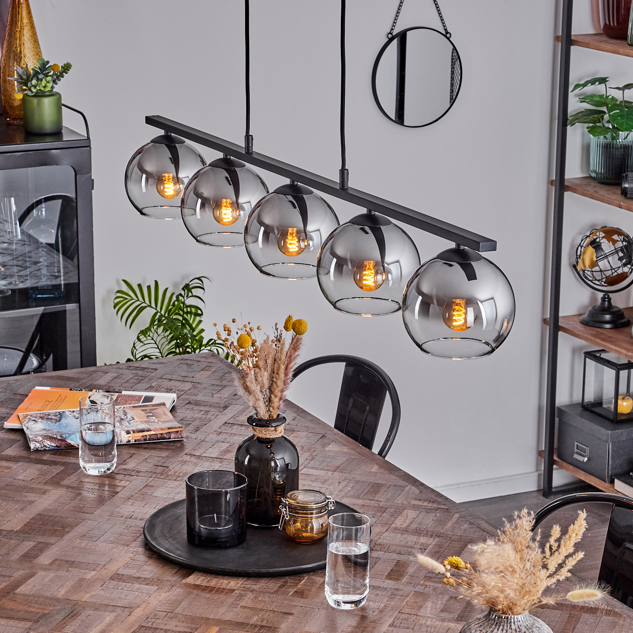 Ein Esszimmer mit Holztisch, gedeckt mit Tellern und Dekoration. Fünf Pendelleuchten hängen darüber.