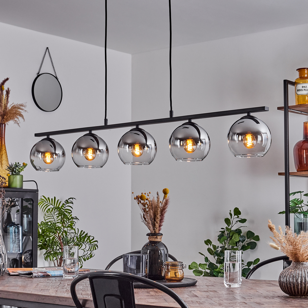 Fünf silberne Kugelleuchten hängen über einem Holztisch, mit Gläsern und einem schwarzen Metallstuhl.