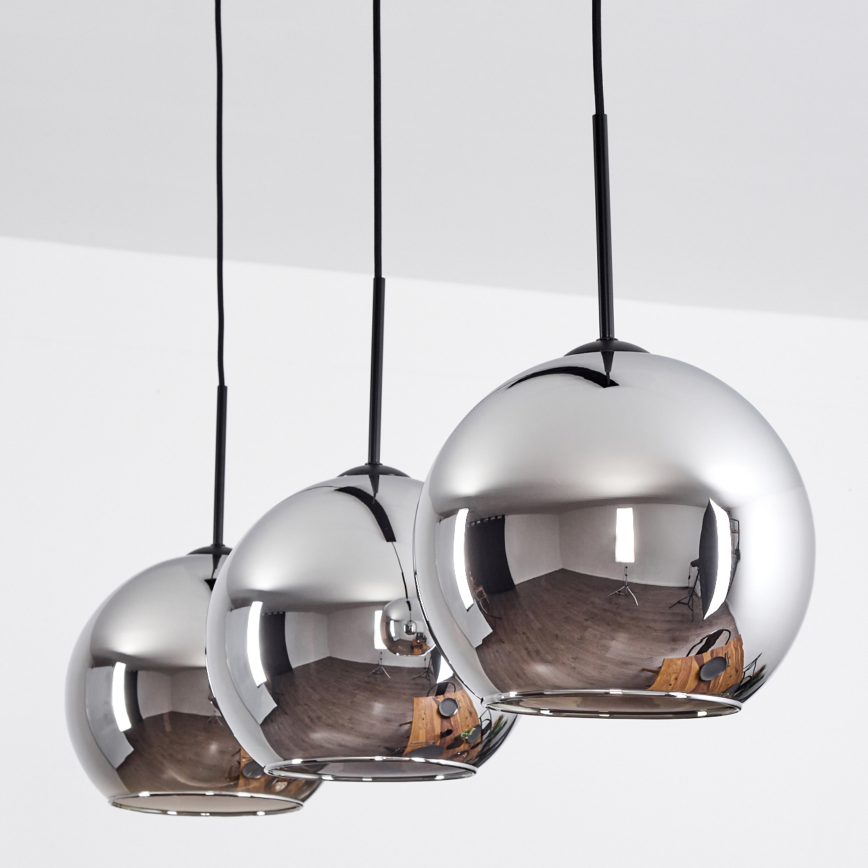 Drei kugelförmige Pendelleuchten vor weißem Hintergrund, die den Raum reflektieren, mit sichtbaren Glühbirnen.